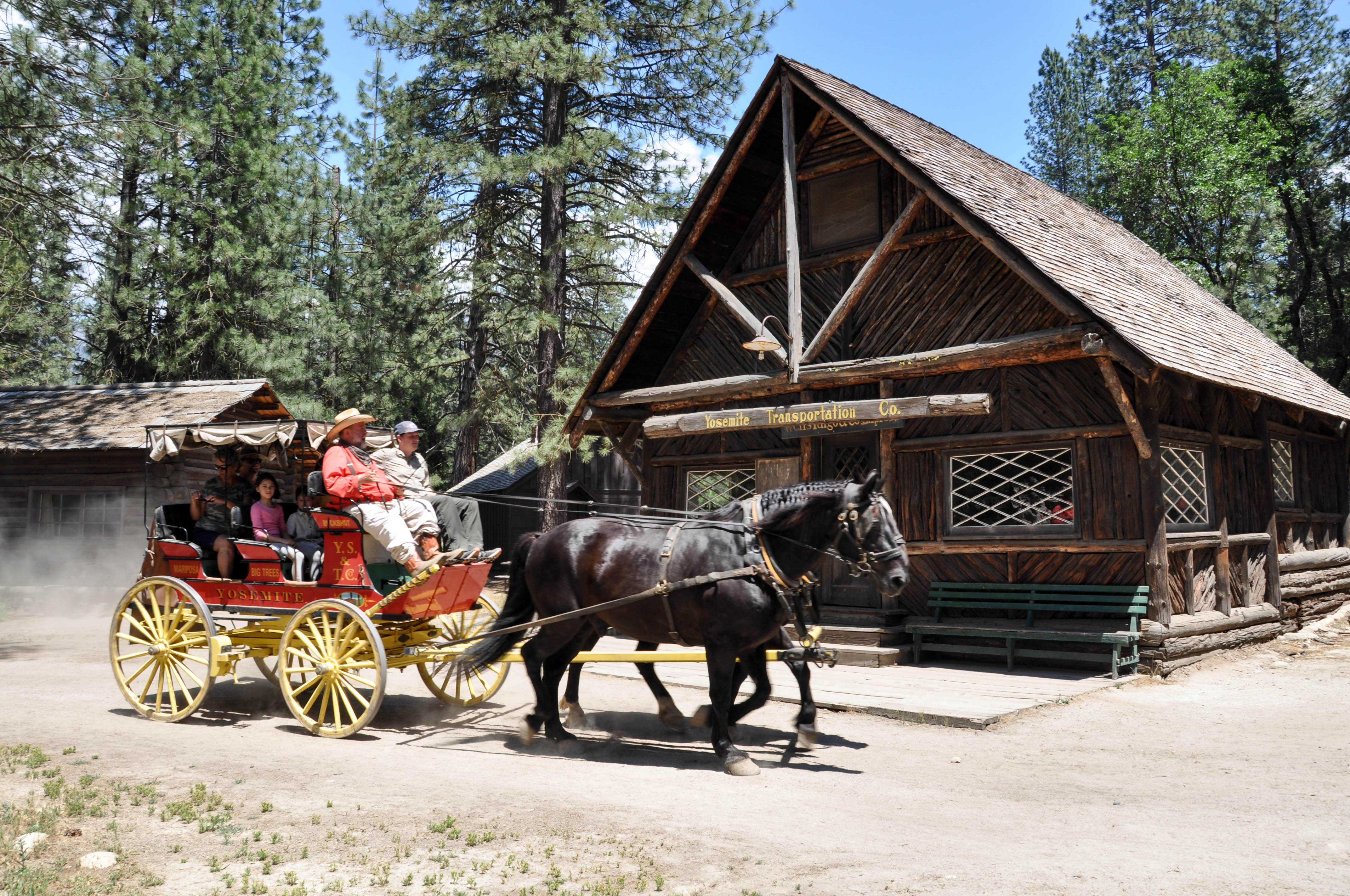 A bright red stage coach with yellow wheels is pulled by a team of two horses.