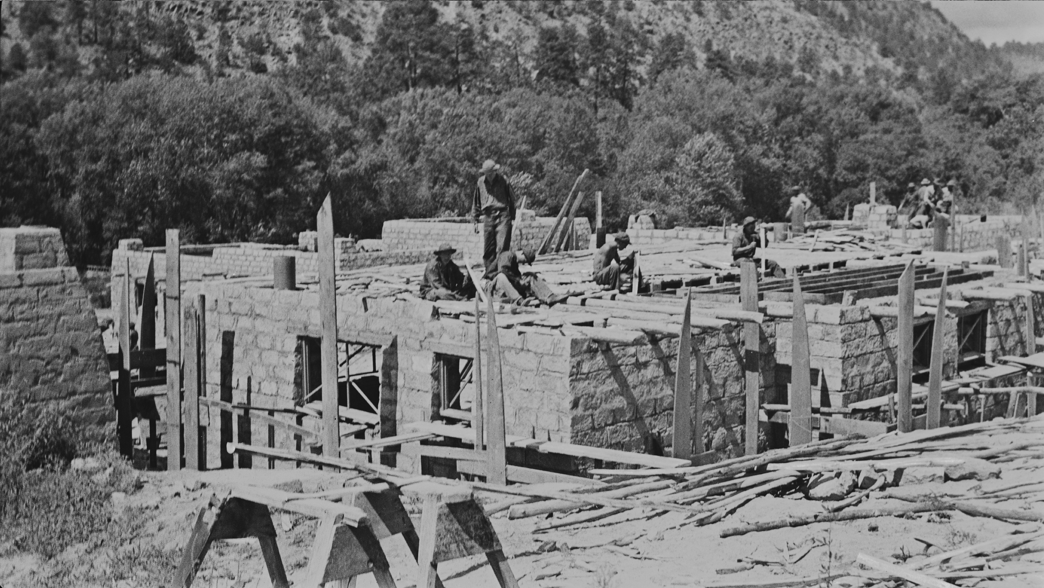 a stone building is under construction, men are working on the roof