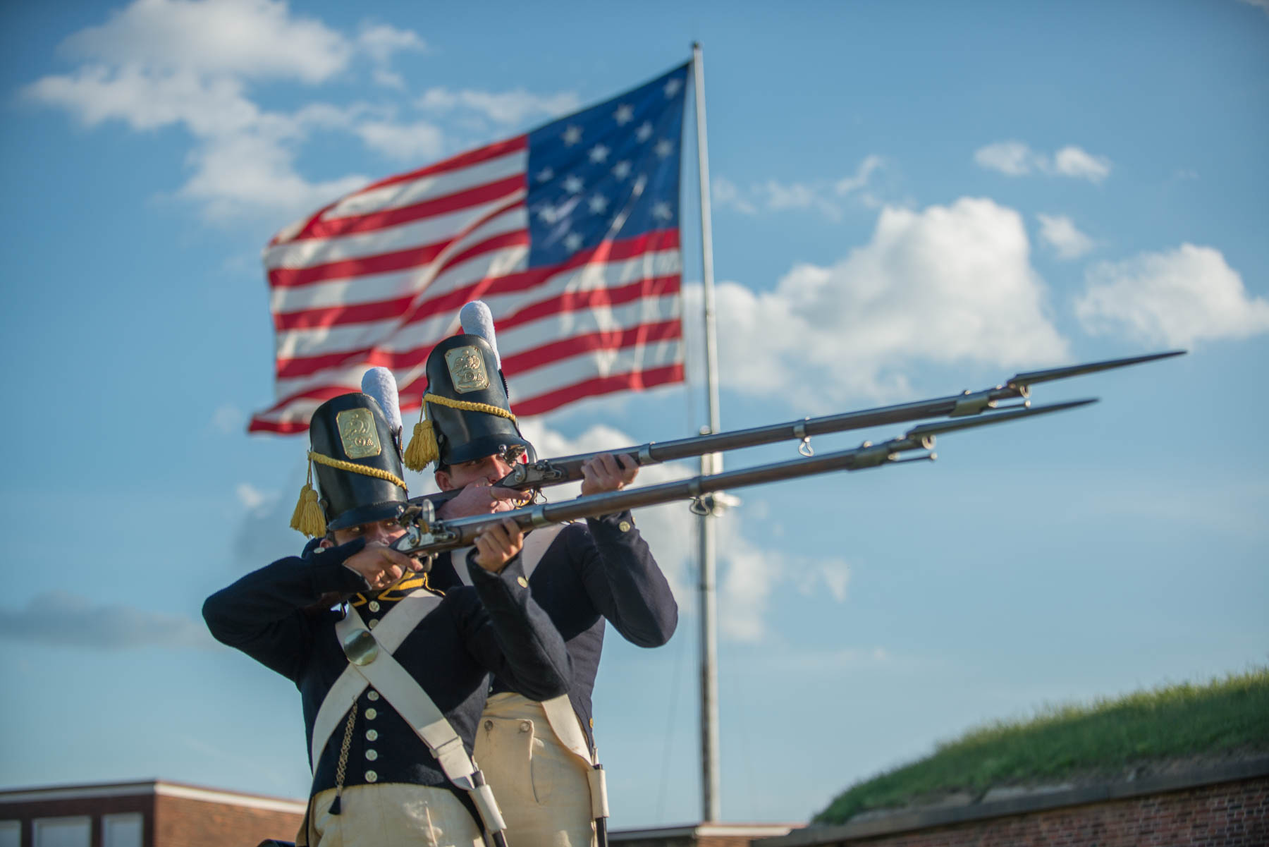 Two living historians in 1812 gear posing in front of the large garrison flag.