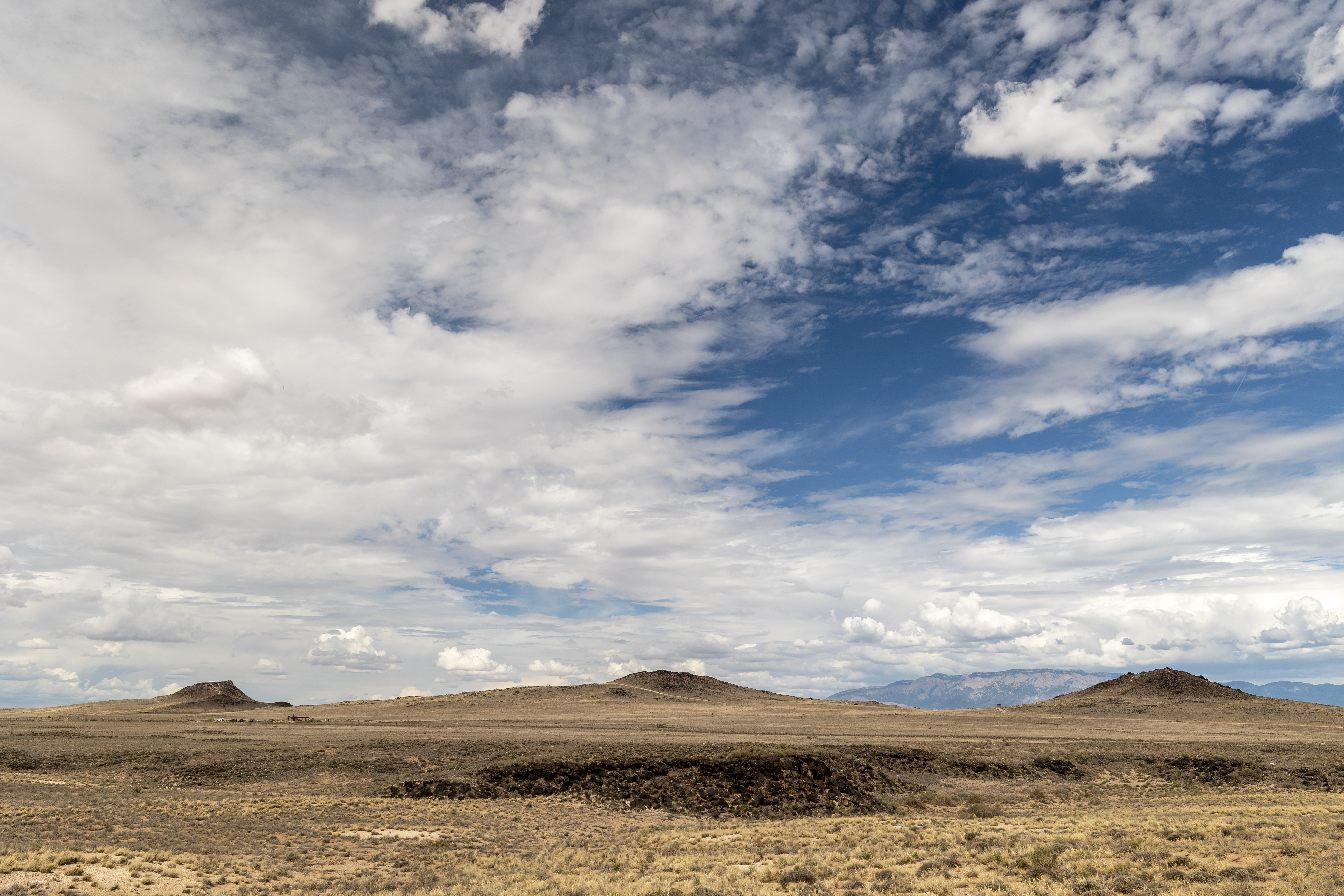 Three volcanoes with a larger mountain in the distance and a partly cloudy sky.