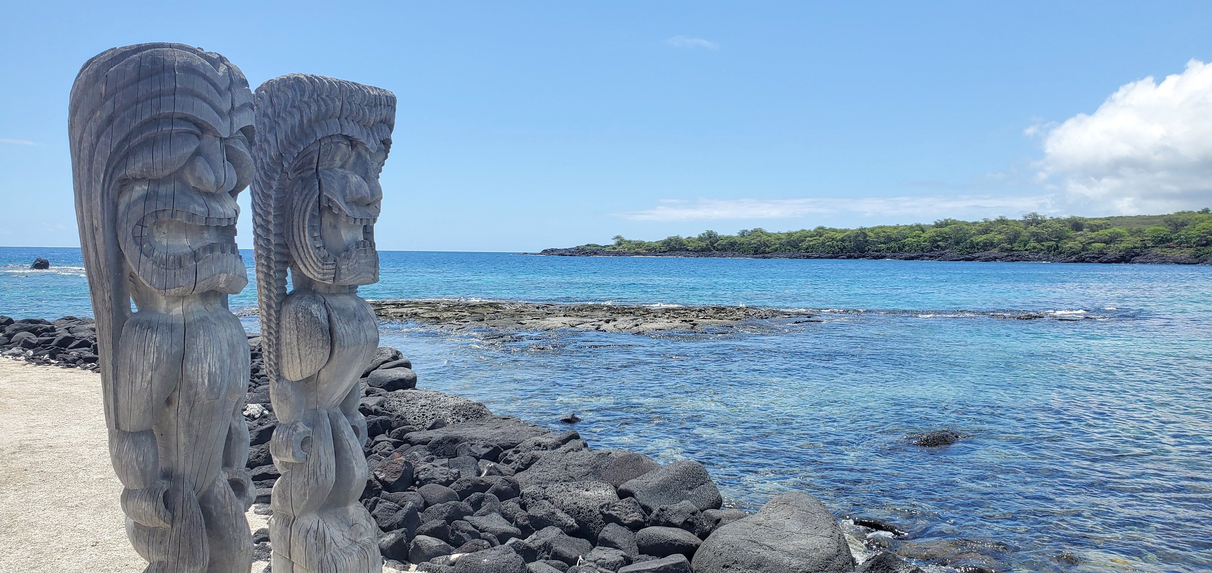 A pair of intricately carved kiʻi (temple images) stand facing Hōnaunau Bay