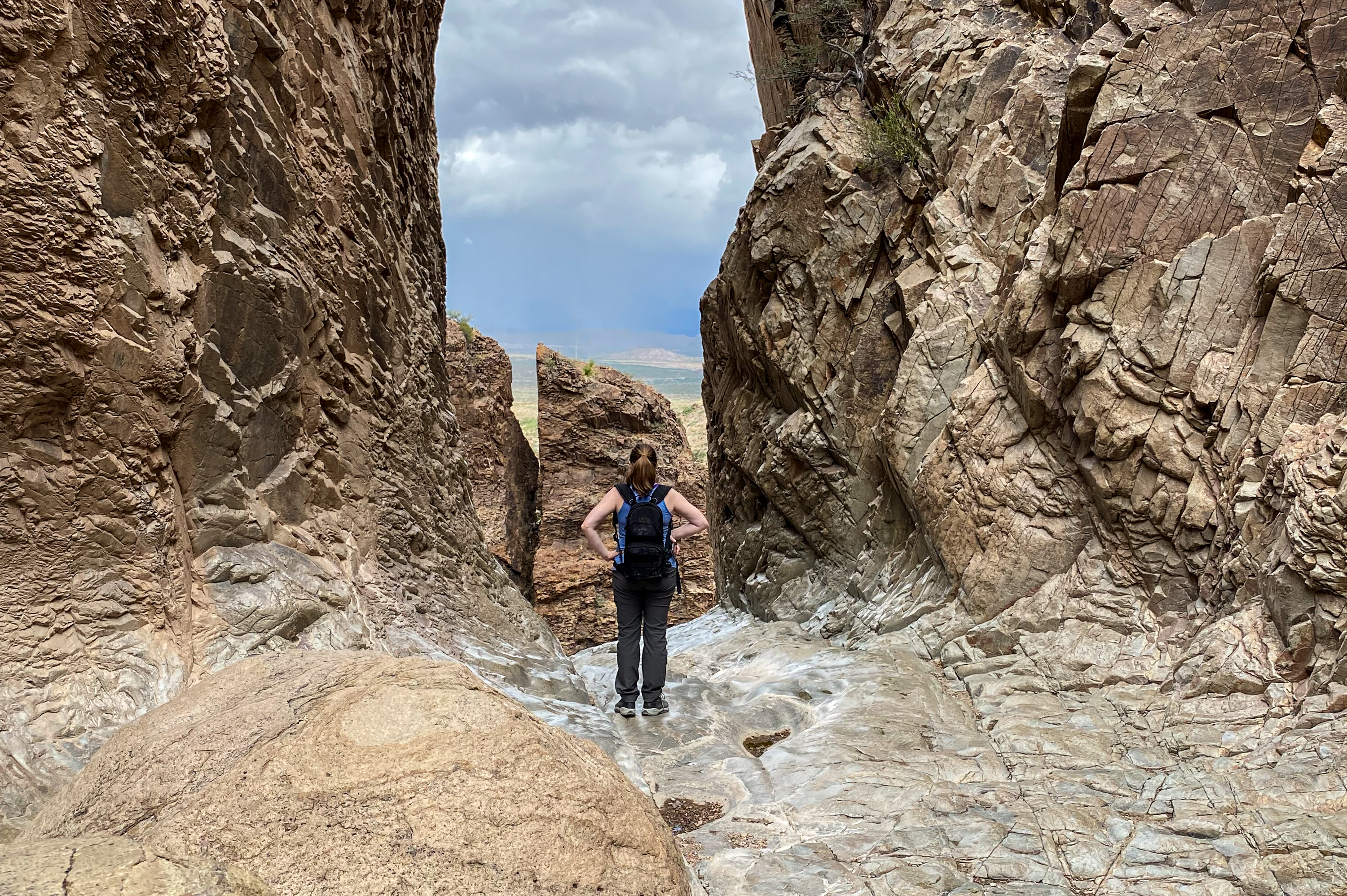 A person stands near the top of a smooth-sided, bedrock pour-off, looking out to the desert below.