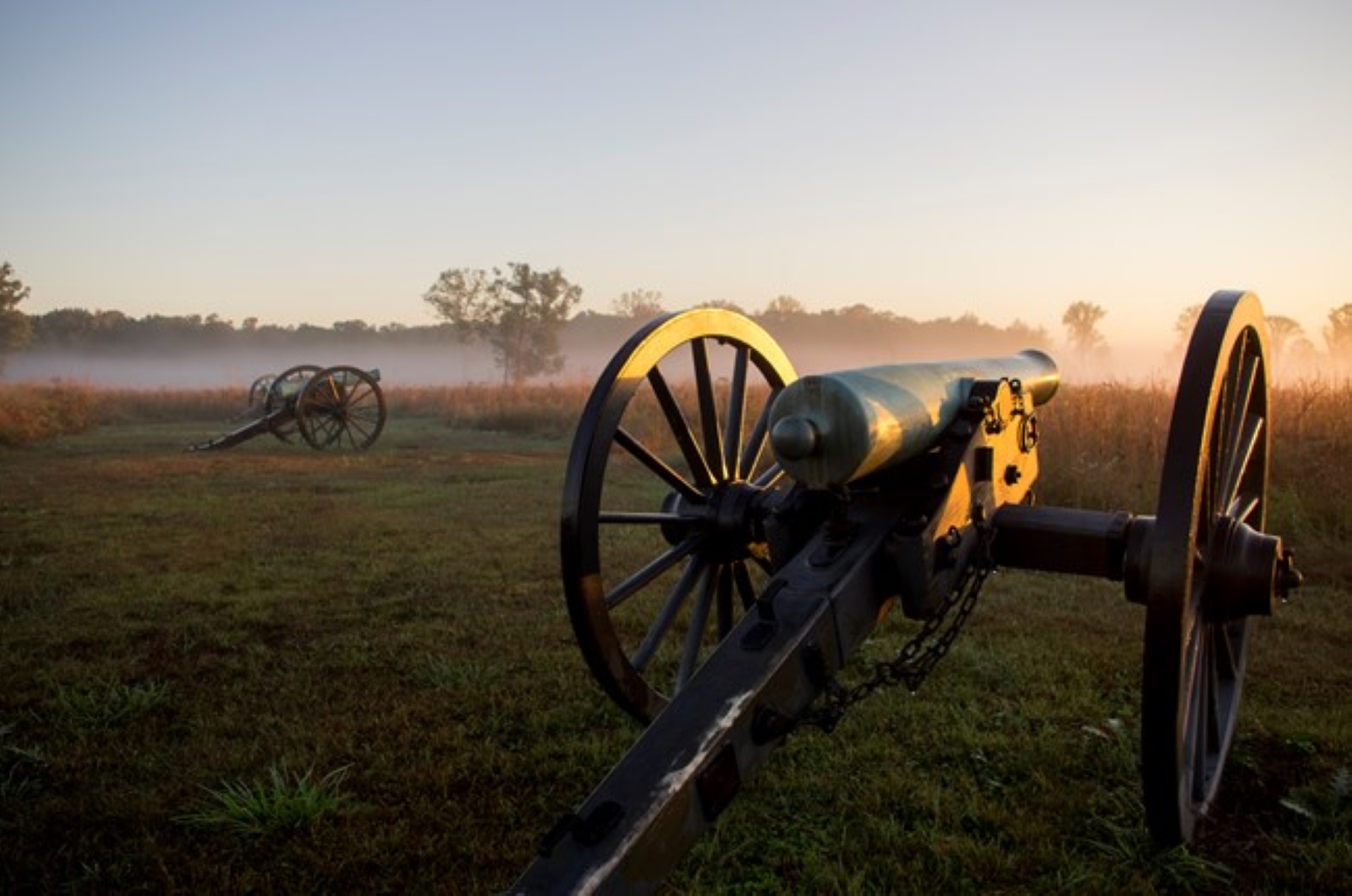 Two cannons sit in a foggy, open field