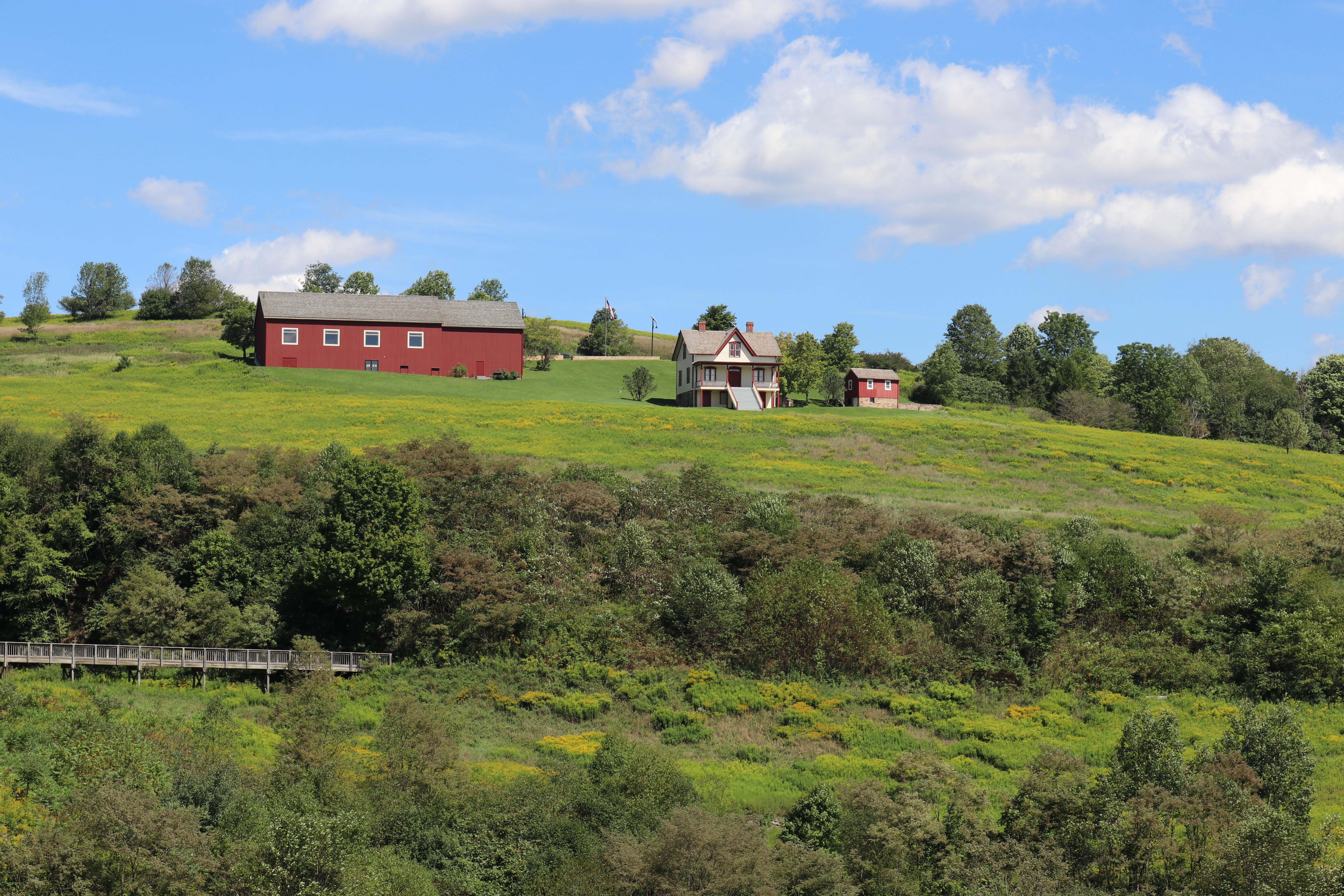 A red barn structure and farmhouse on the hillside.