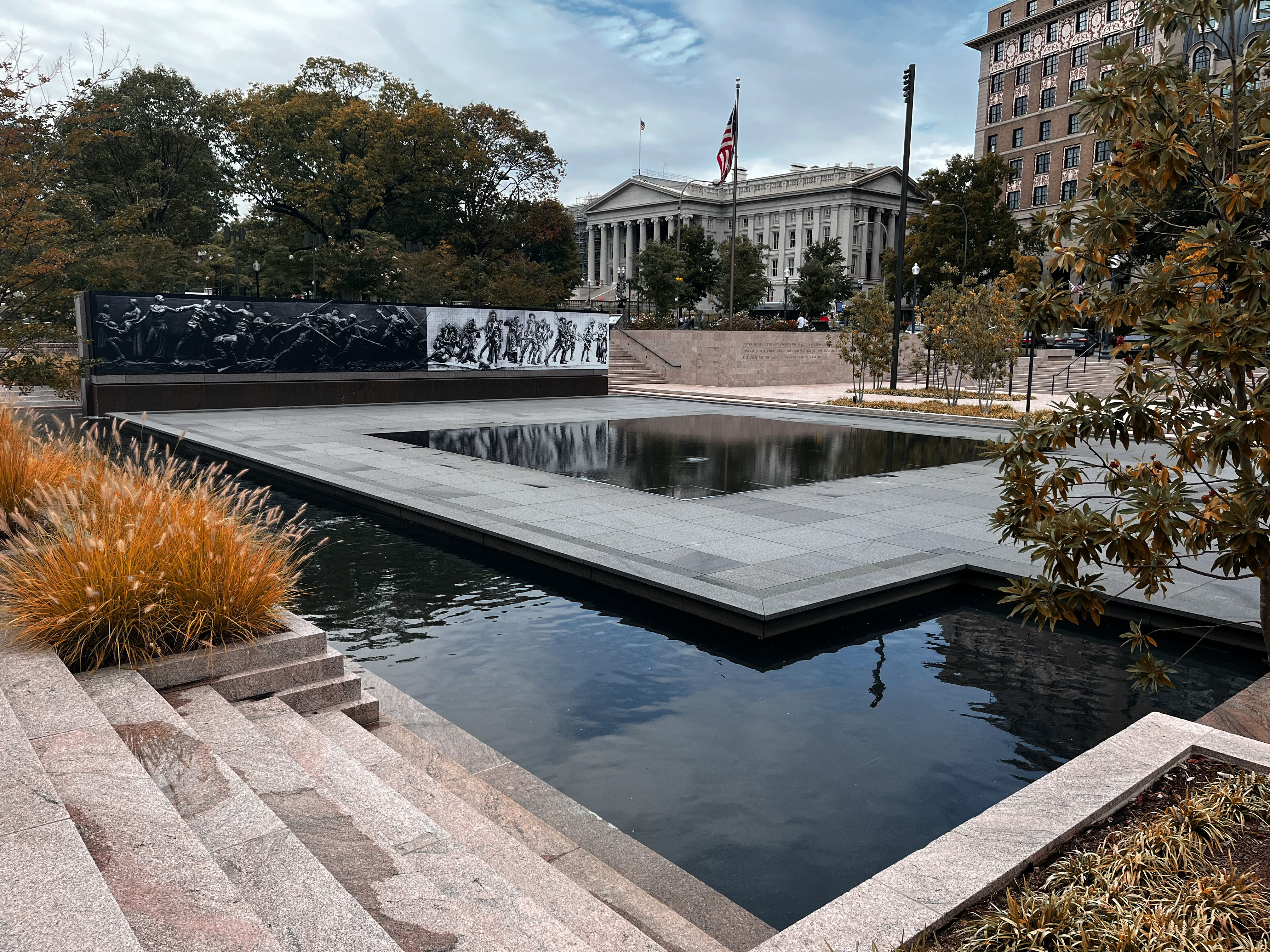 The picture features a water feature with still water in the center of a stone square.