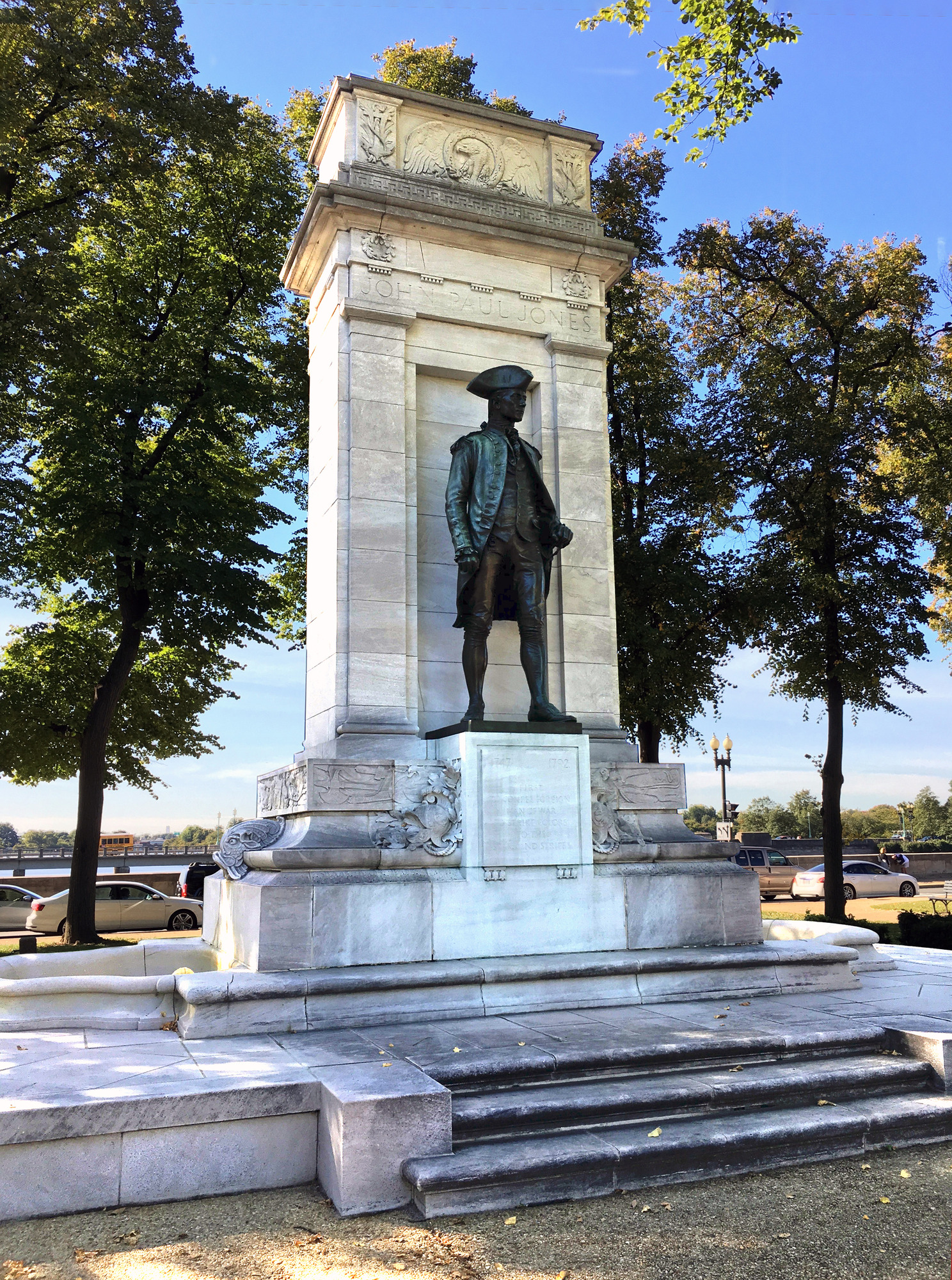 A monument featuring a dark bronze , standing figure atop an ornate stone base.