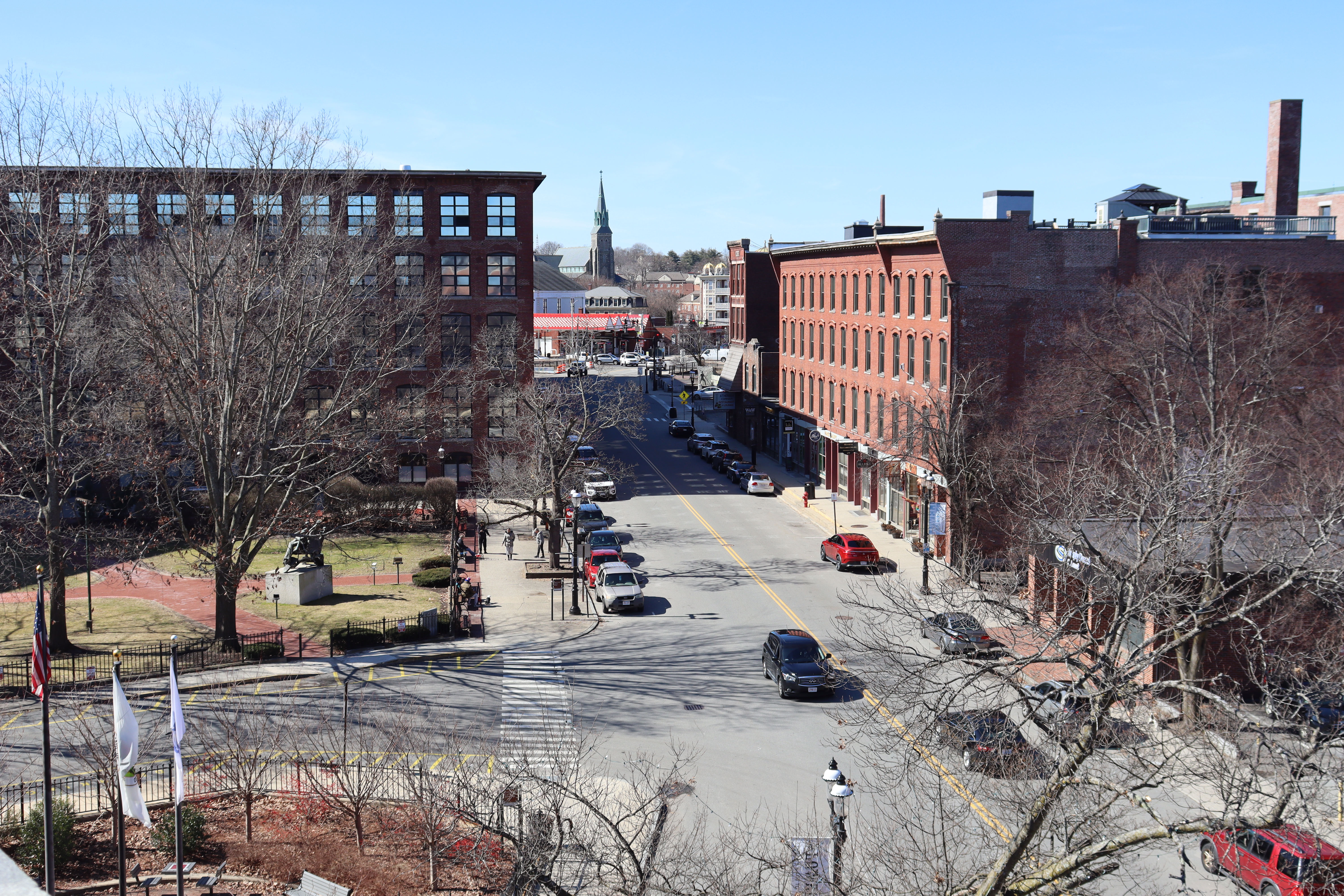An overhead street view with cars parked along both sides of the street and several brick buildings.