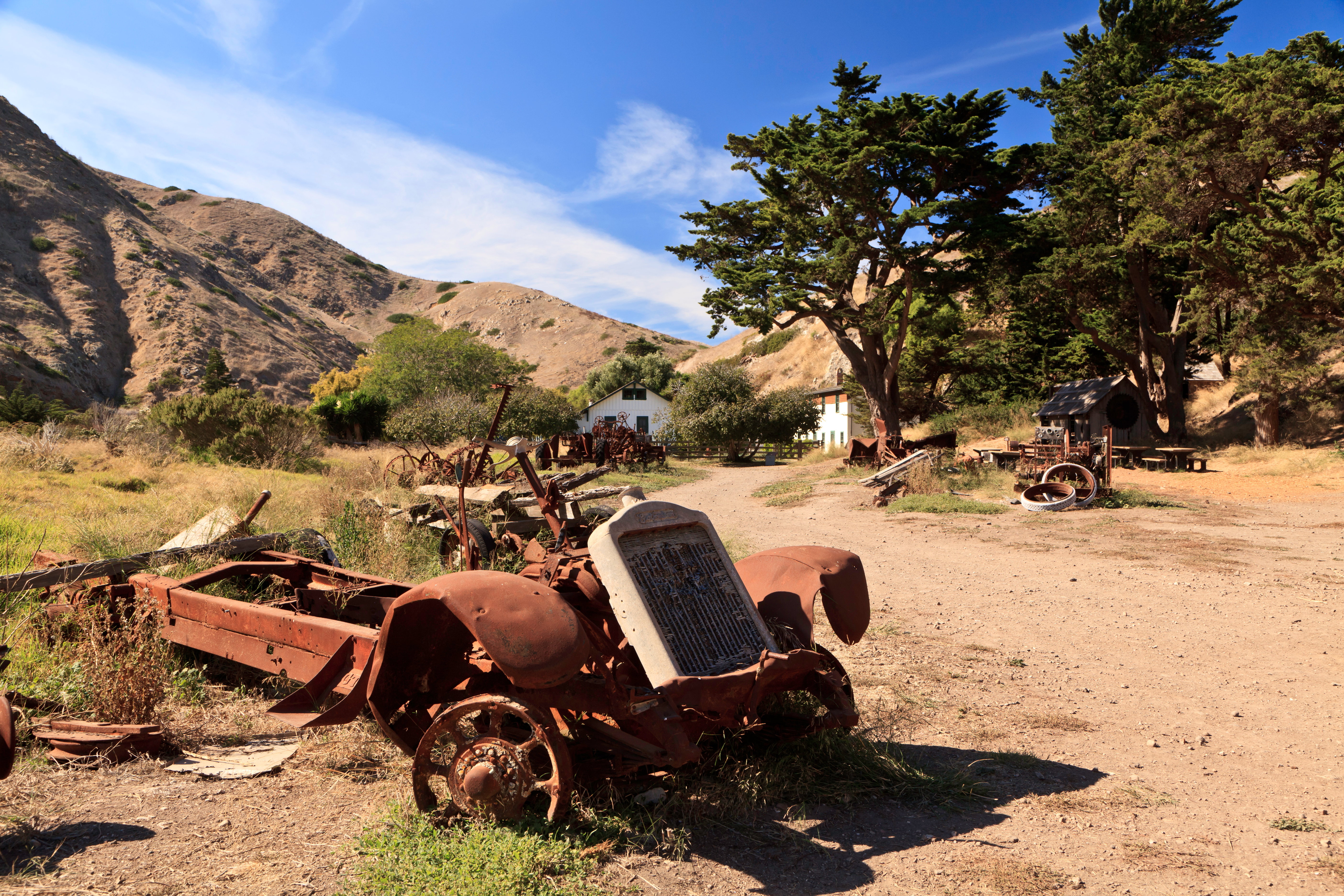 rusted farm equipment in front of ranch house