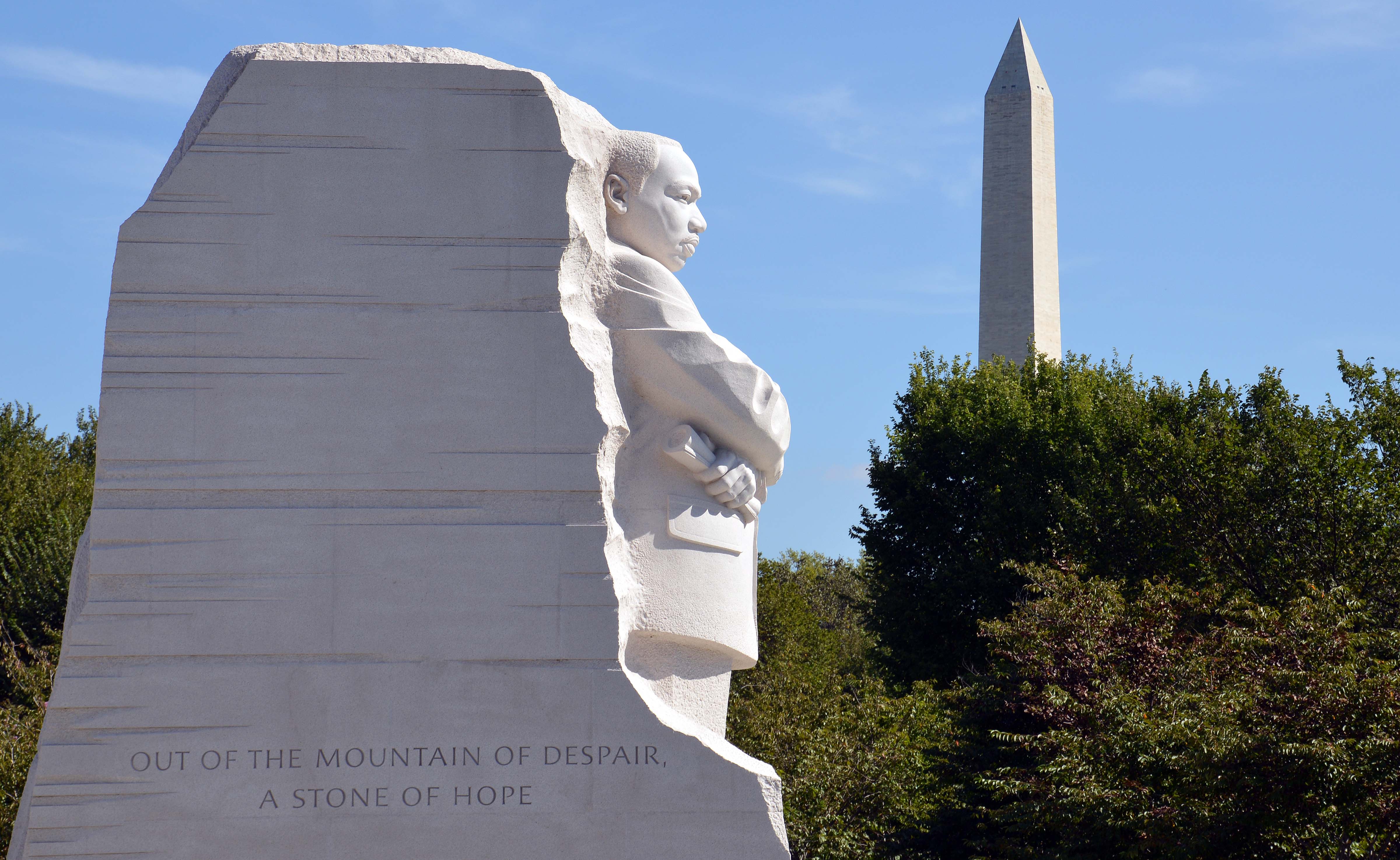 Tall white structure with man carved into the front next to a tall white obelisk