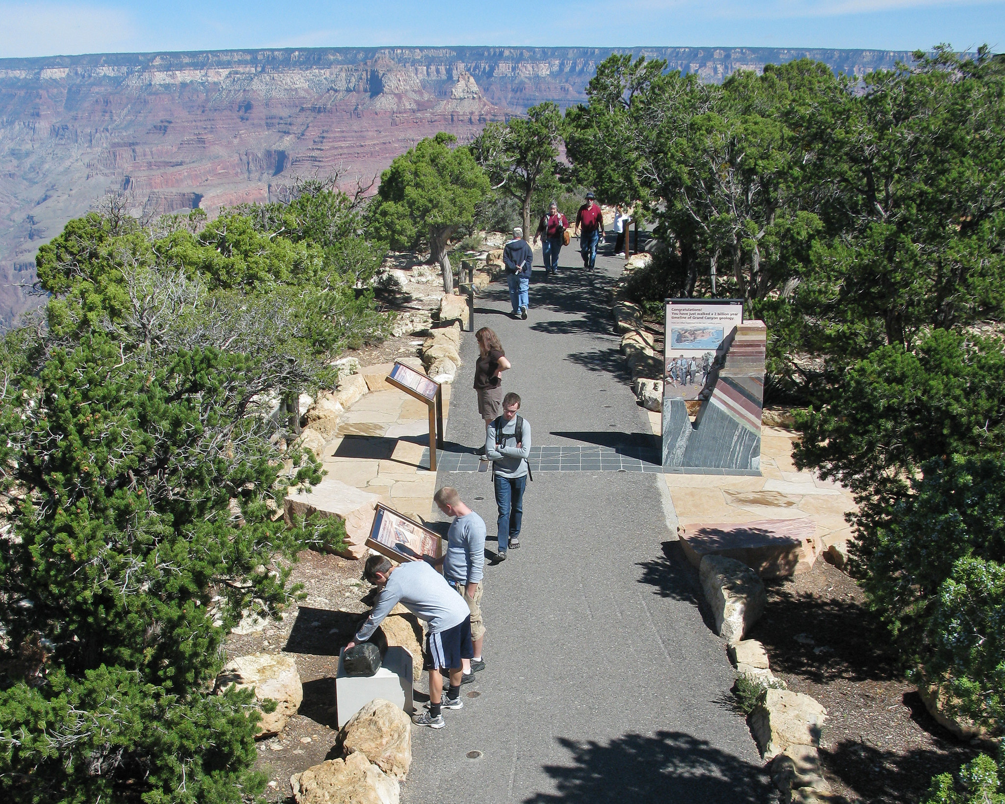 A paved path lined by exhibits and people next to Grand Canyon