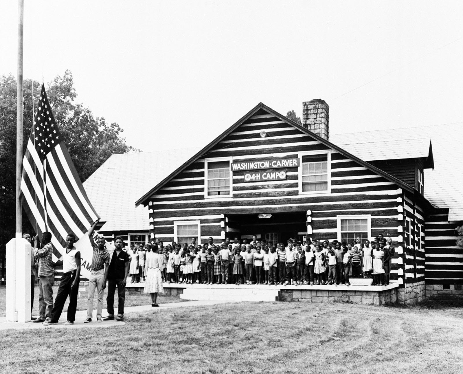 campers raise a flag in front of a camp lodge