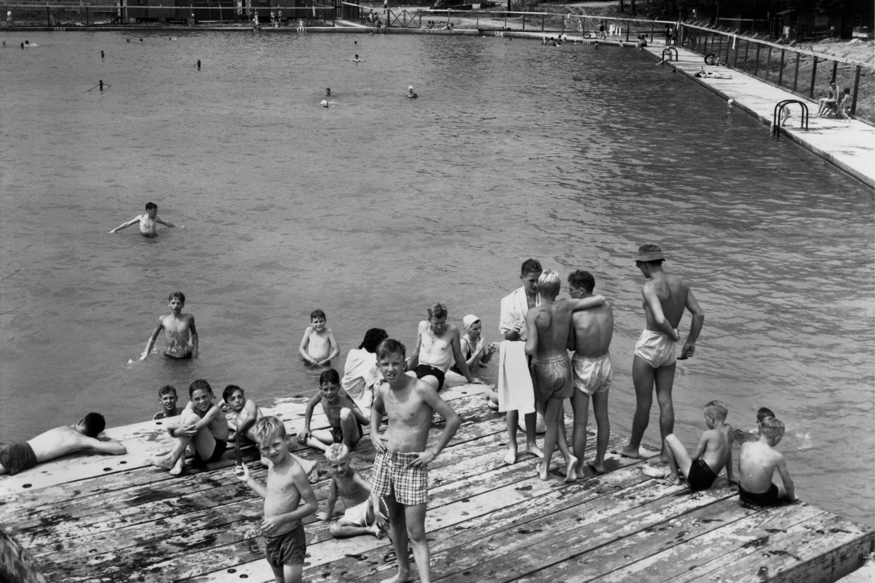 Black and white photo of several young people in swimsuits gathered on a wooden platform at a pool