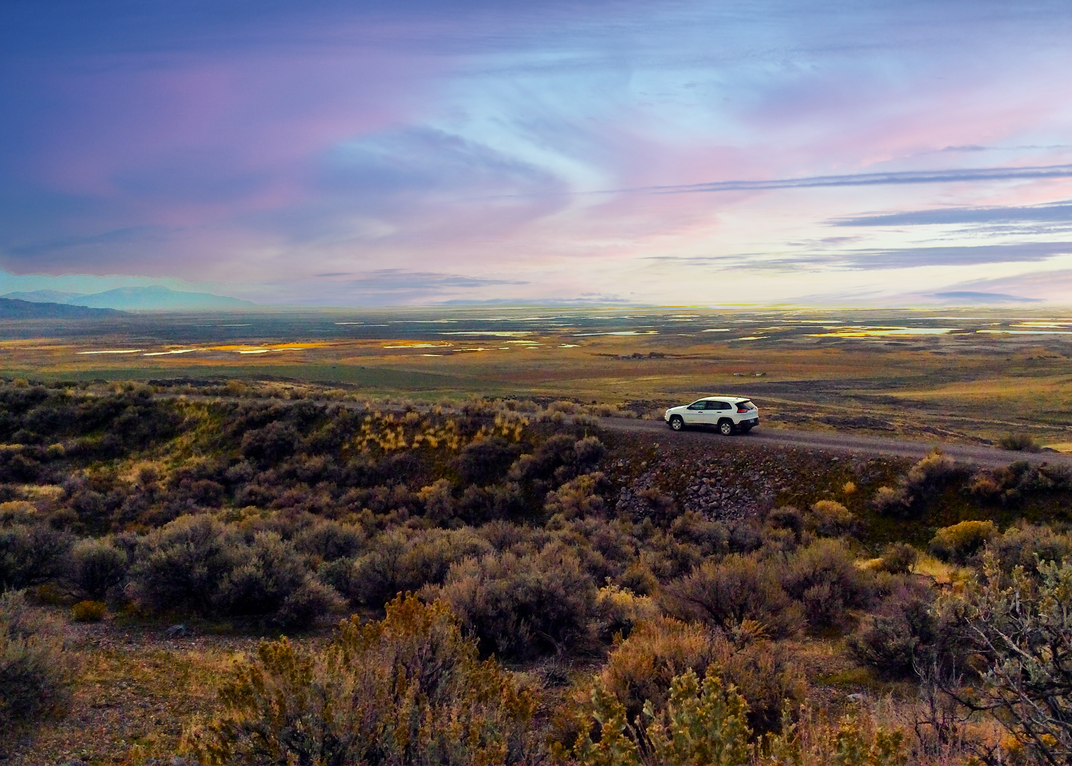 Gravel road through a landscape of brown, yellows, oranges with a sky of purple and blue