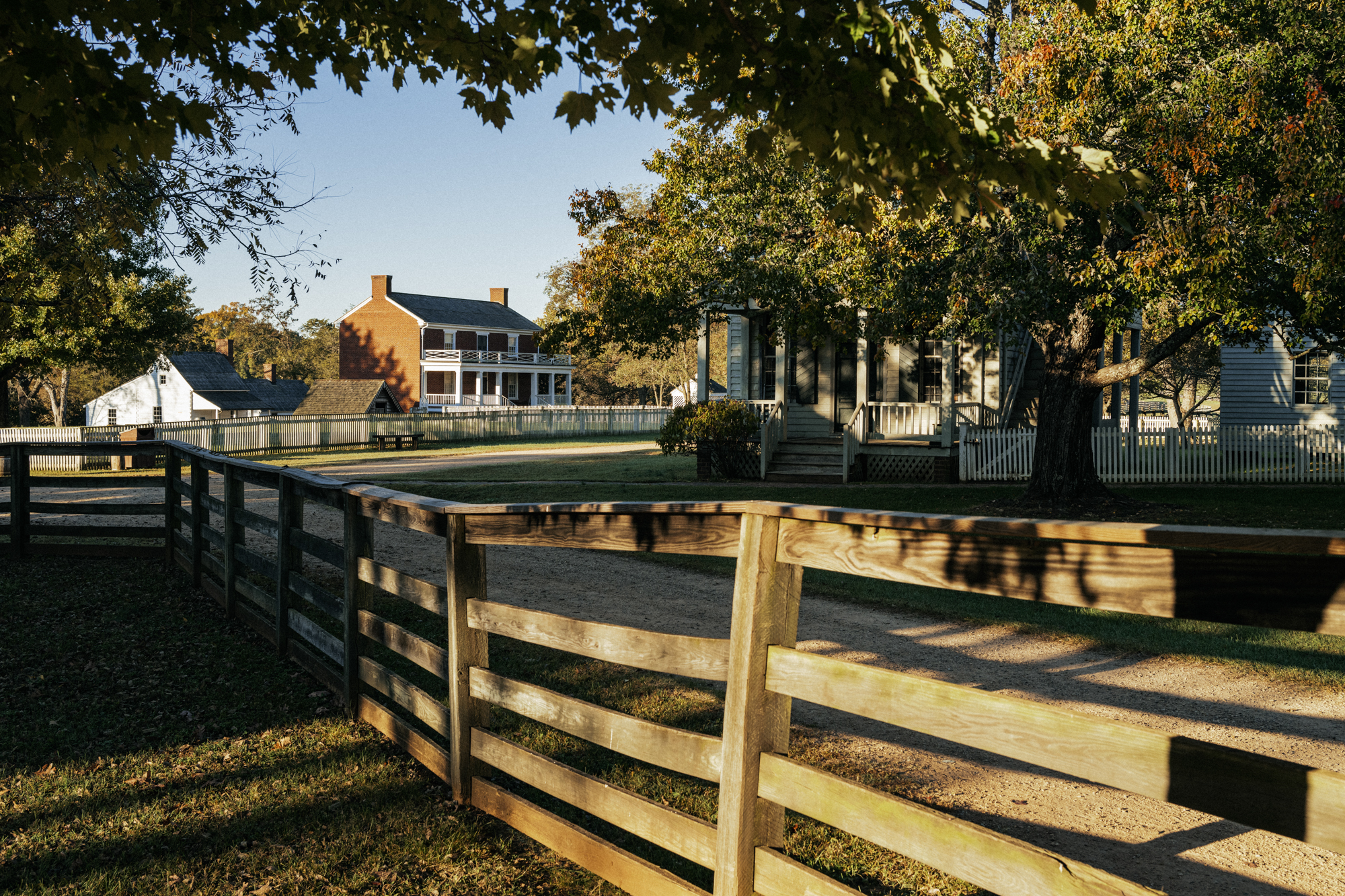 A wooden fance lines a dirt path. The McLean House complex is in the background.