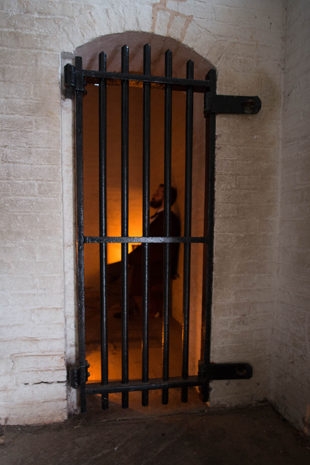 A man in 19th century clothes in a jail cell.