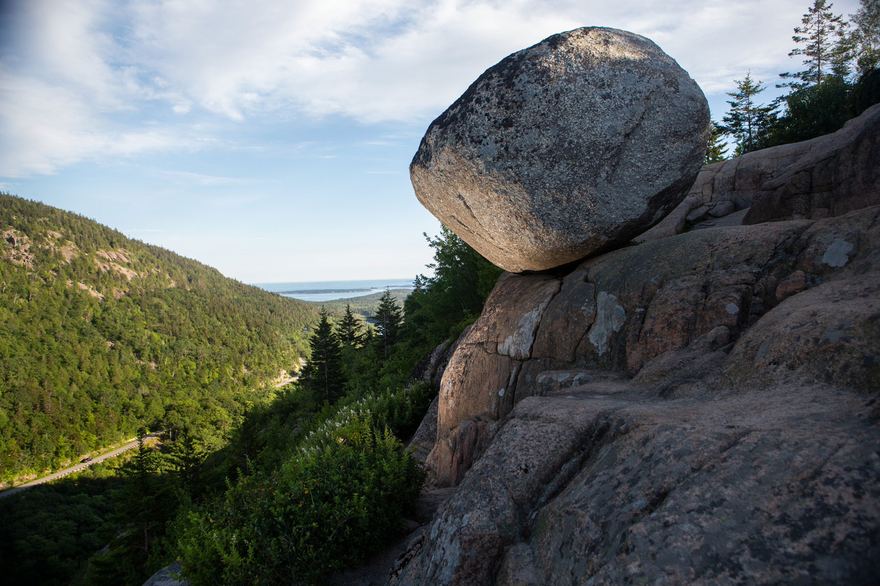 a large round rock perches on the end of a mountain