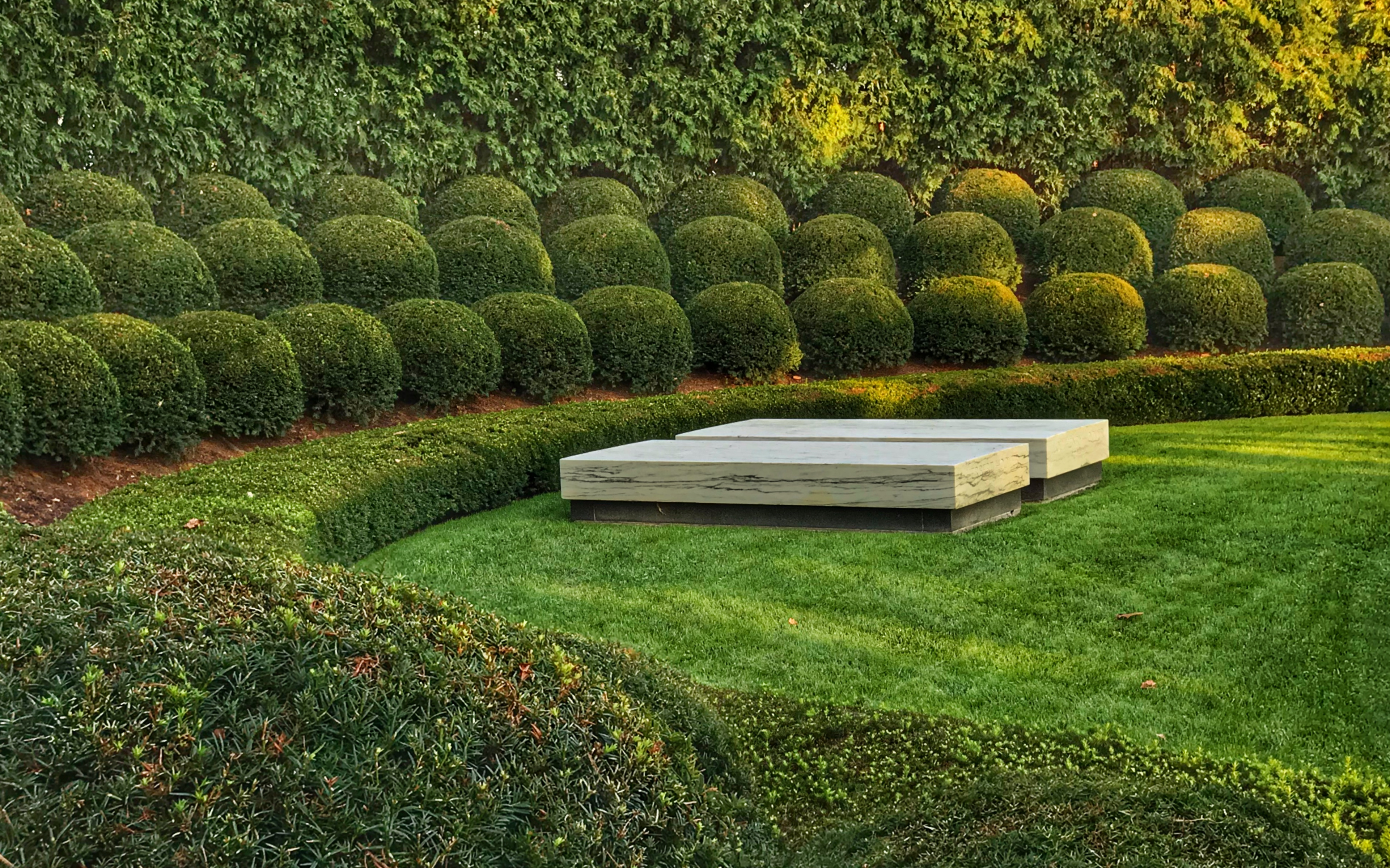 Rows of neatly trimmed bushes and trees form an arc around two marble slabs marking graves.