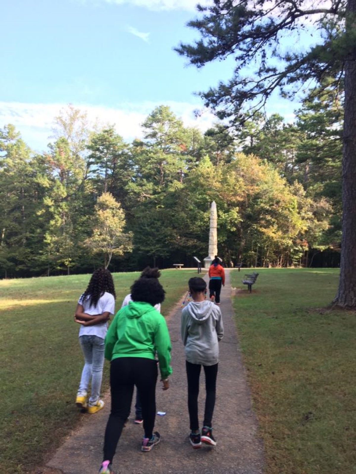 Five African American children walk on a path to a monument at the end of the trail.