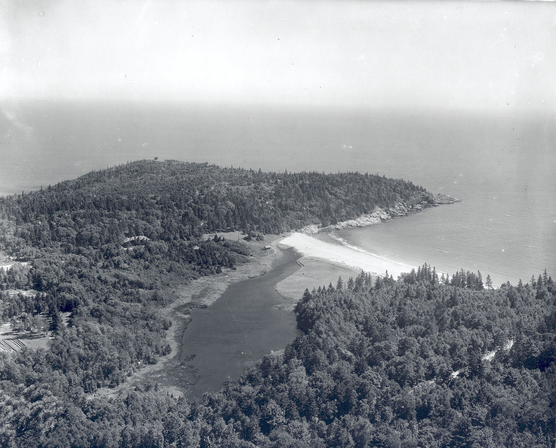 a spit of land covered in trees protects a sandy beach from the atlantic ocean.