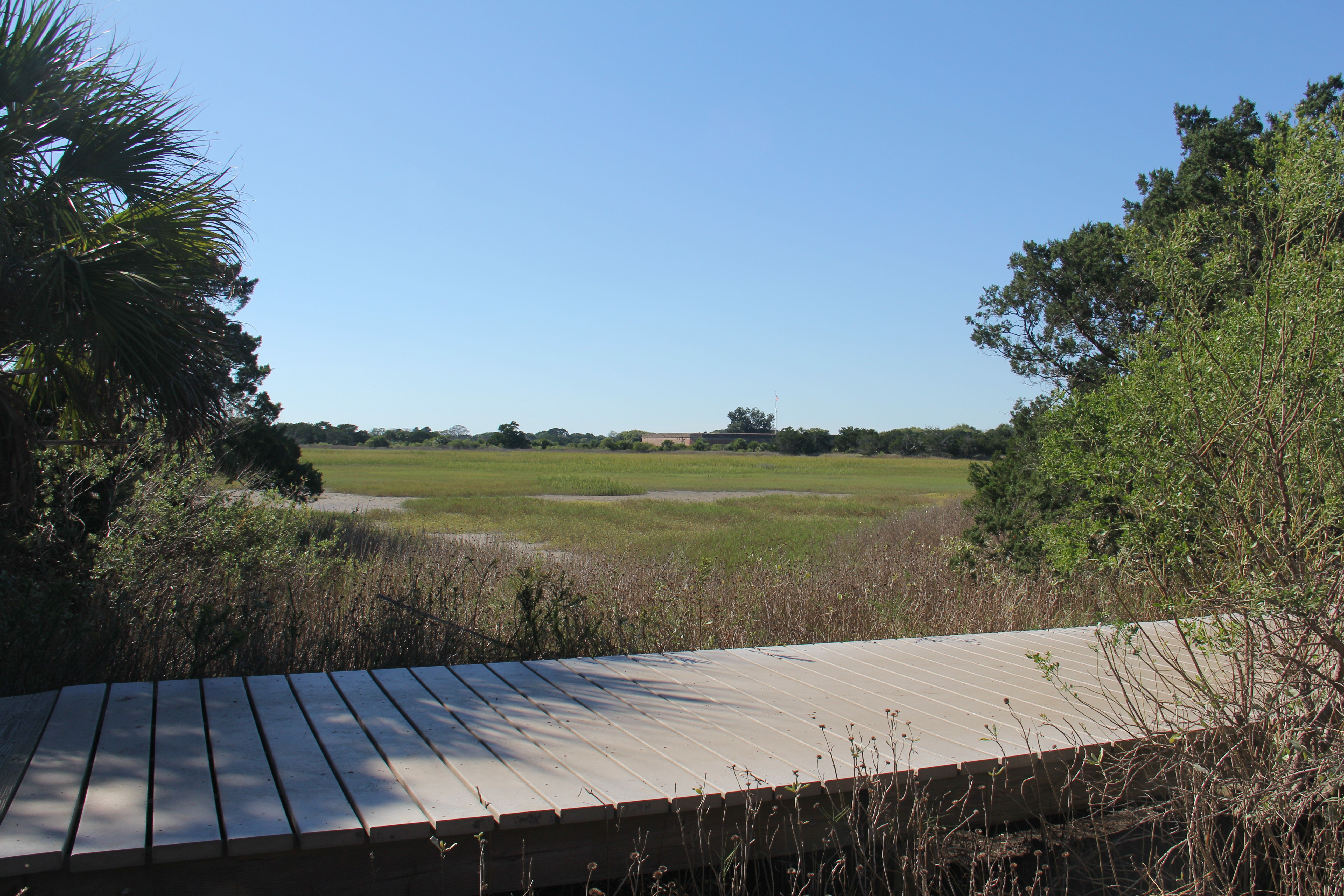 A boardwalk over a marsh with a large brick fort in the distance.