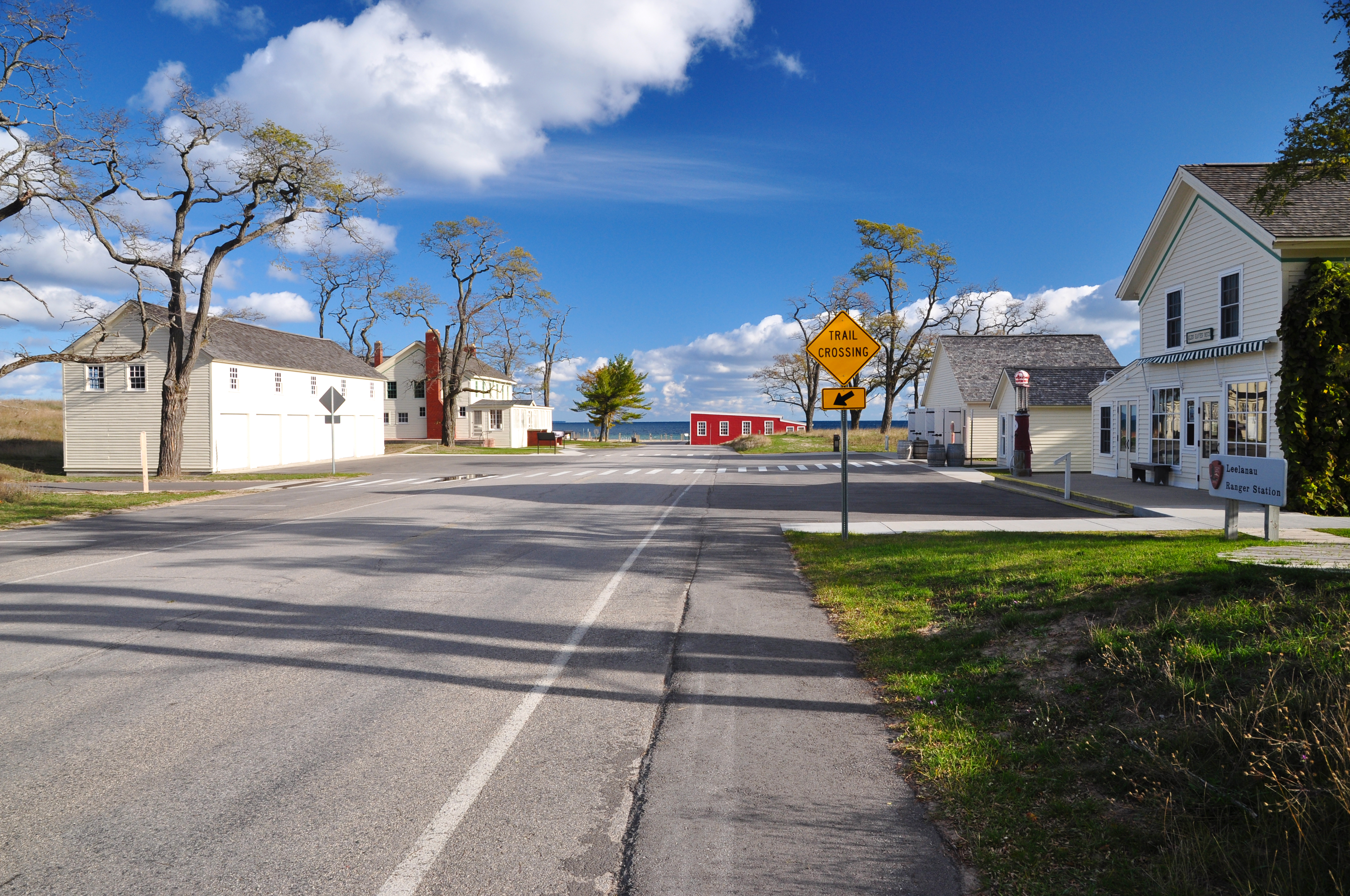 White, gabled buidlings line the road that leads to a bright, red, low building on the lakeshore.