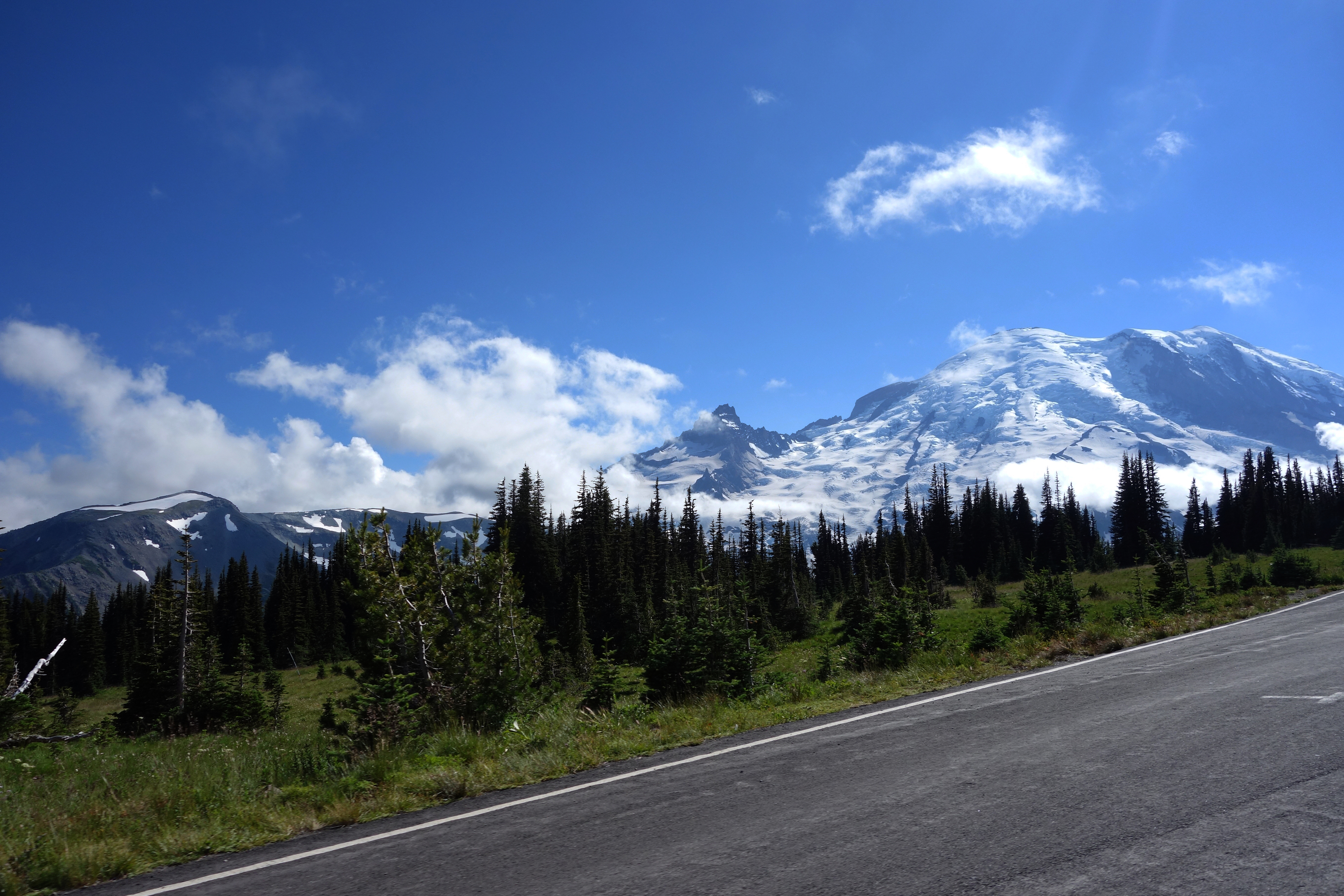 A glaciated mountain rising above subalpine meadows next to a road.