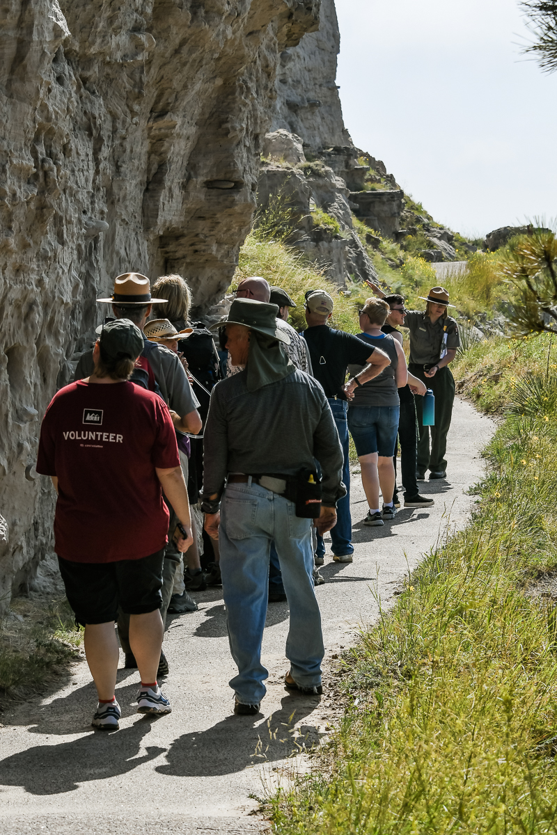 A park ranger points to a rock cliff while a group of people observes.