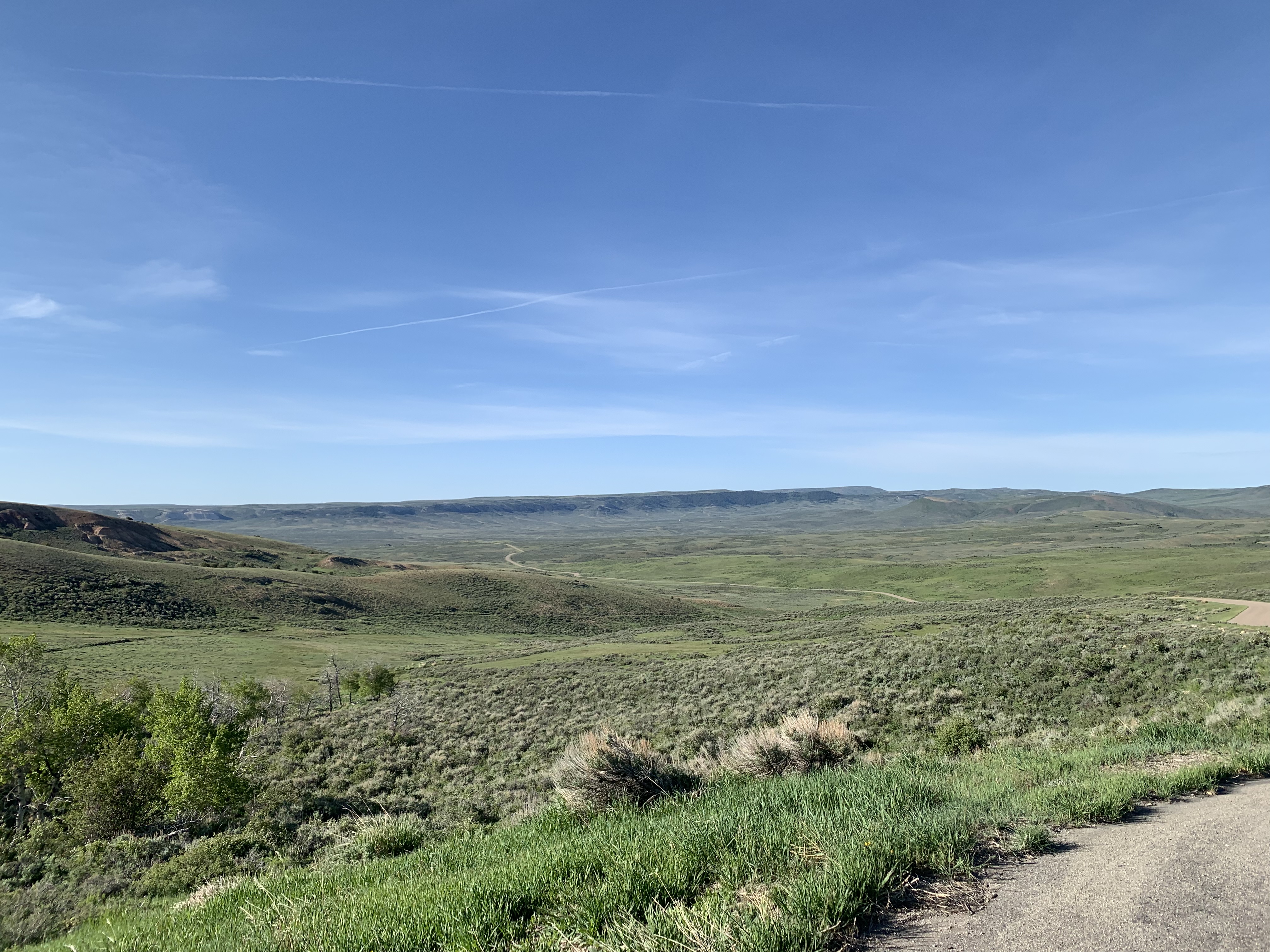 The road leads away through mildly rolling hills of sagebrush and green grasses.