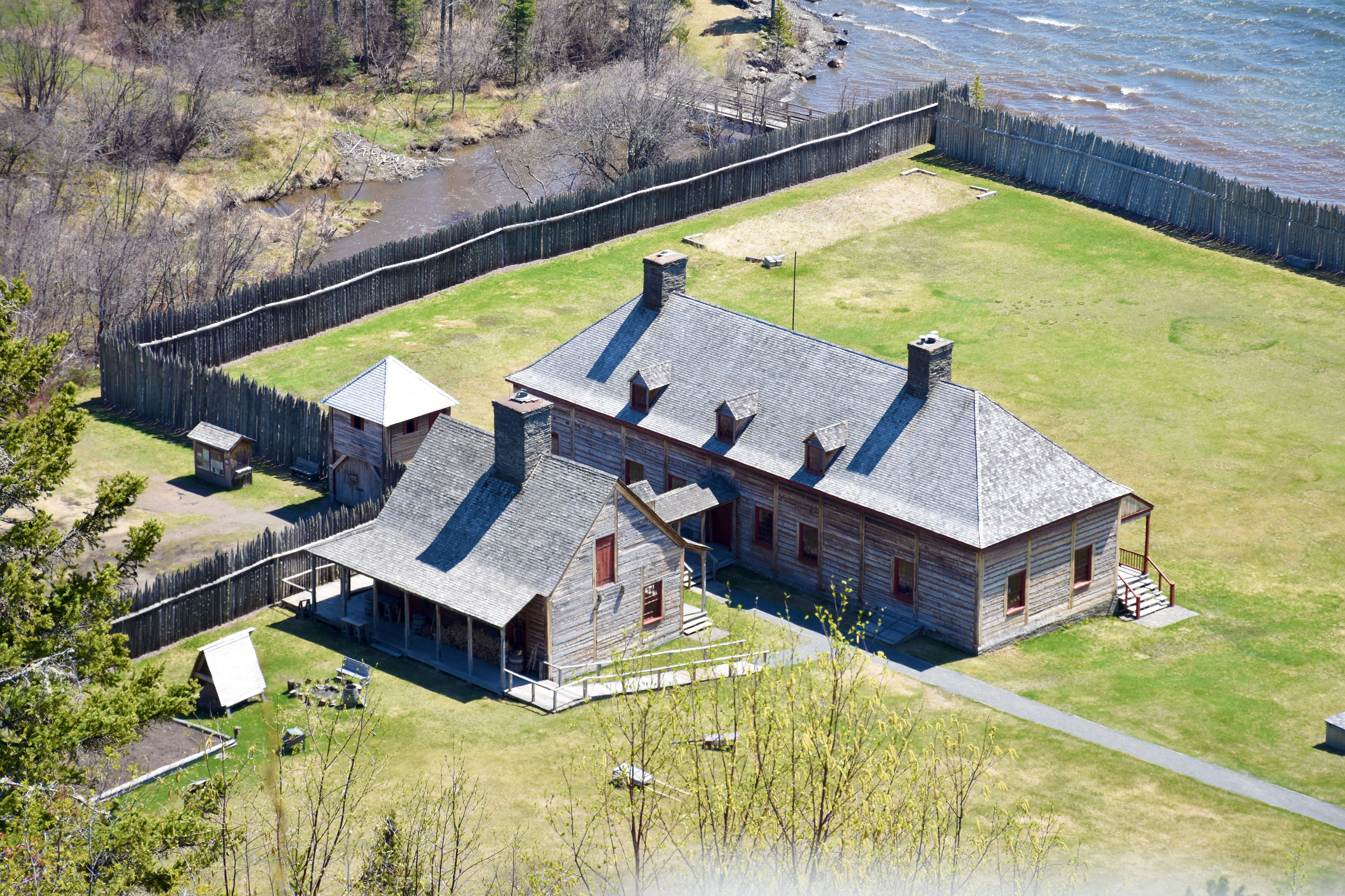 Historic buildings within a stockade, adjacent to a creek that empties into a lake.