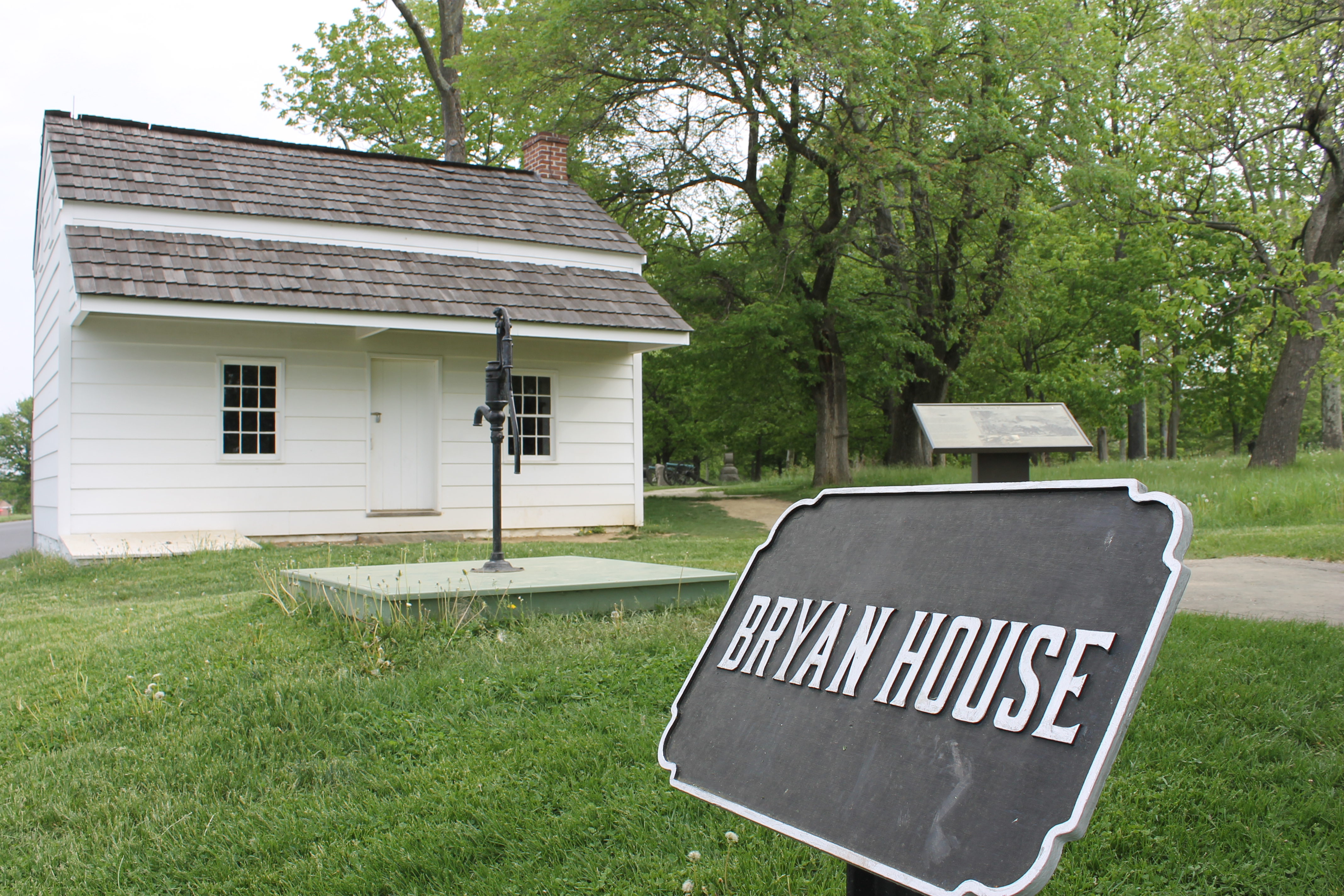 Small white one story home with white wood paneling. A black and silver marker reads "Bryan House."