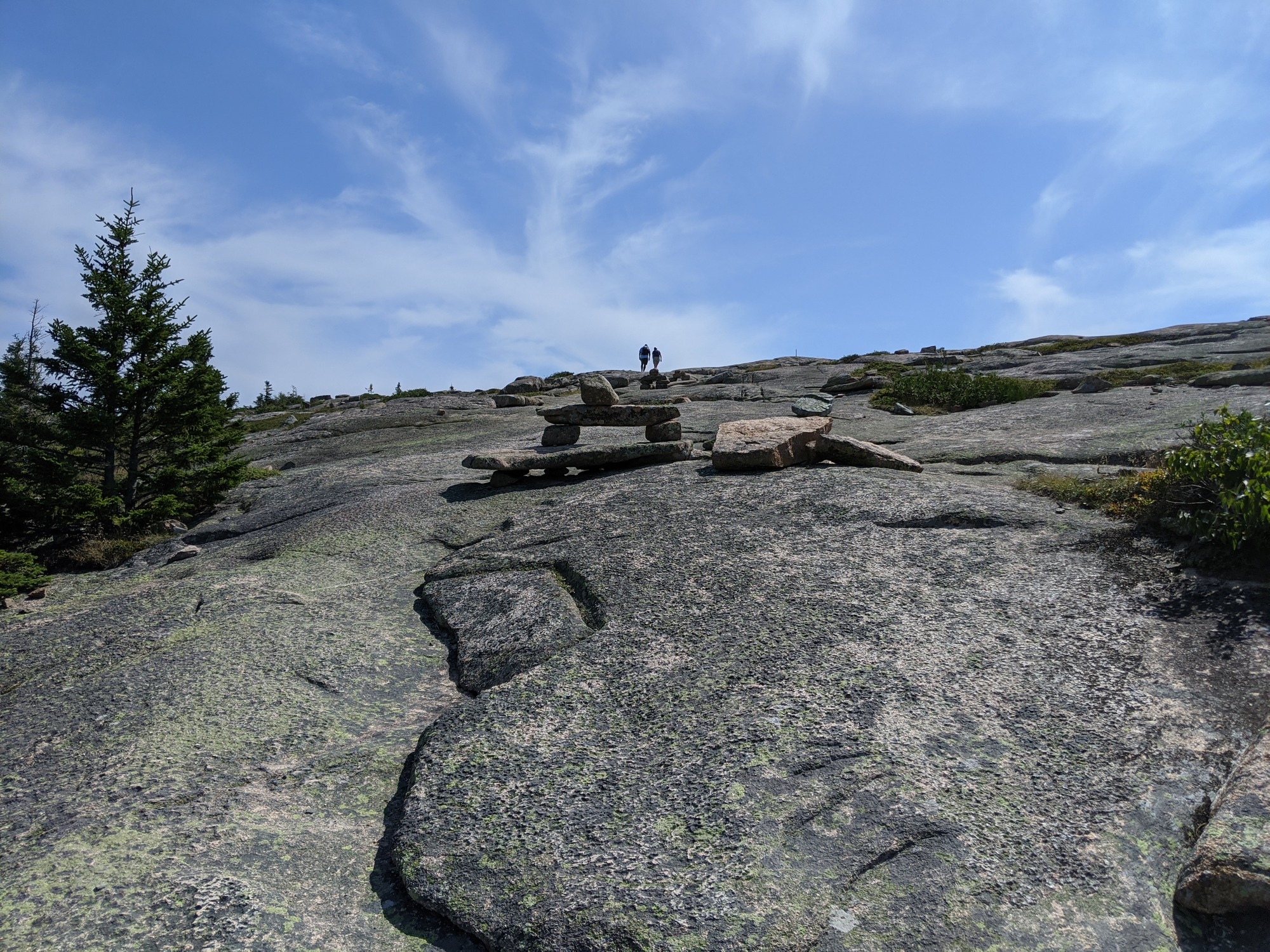 Granite slab with a Bates Cairn in the distance and two figures walking.