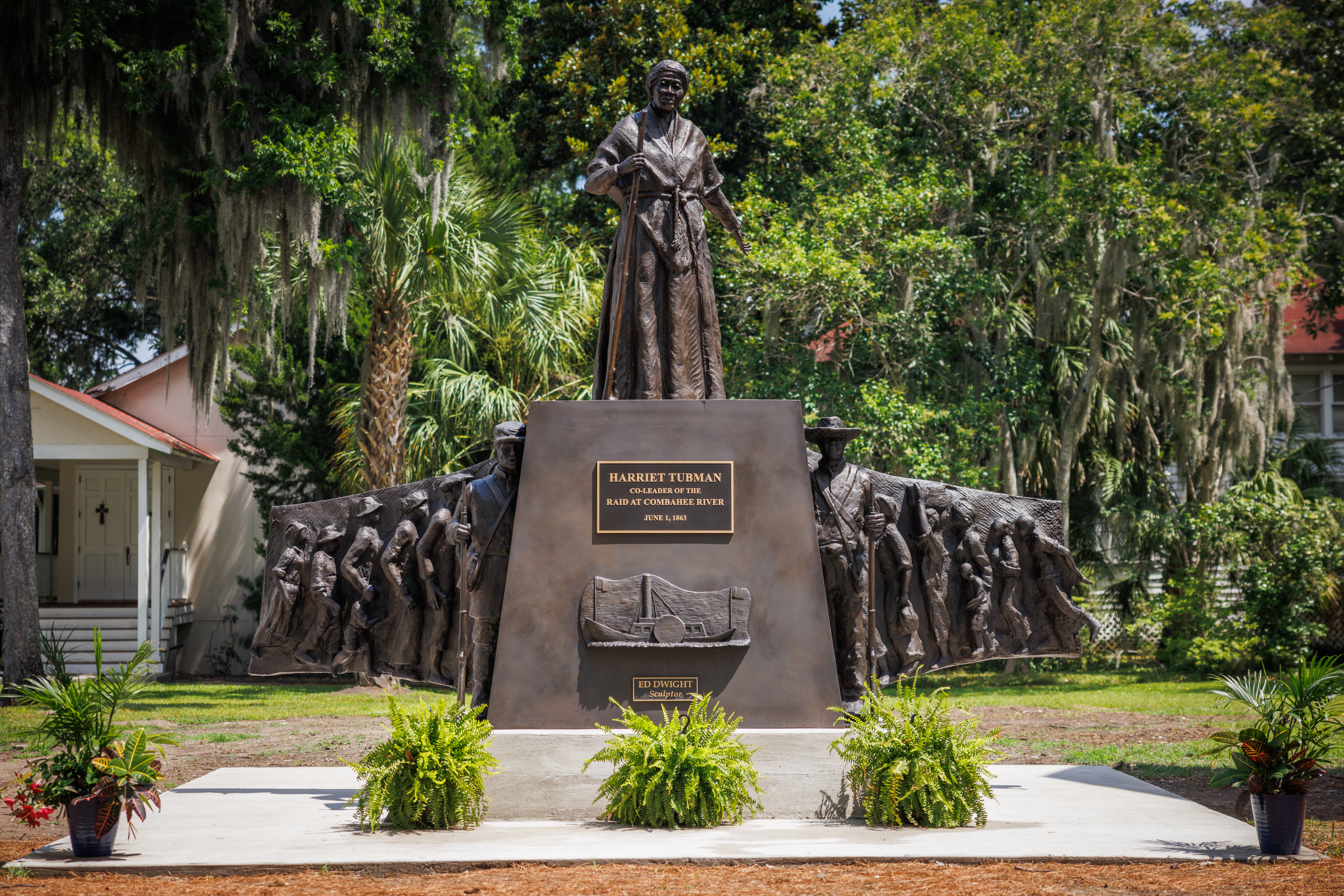 A bronze statue of a woman standing with two soldiers on each side and people running to them.