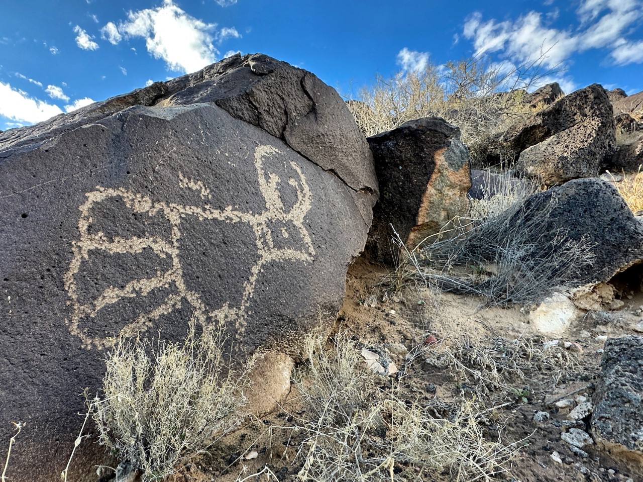 A rock carving on a dark boulder under a blue sky.