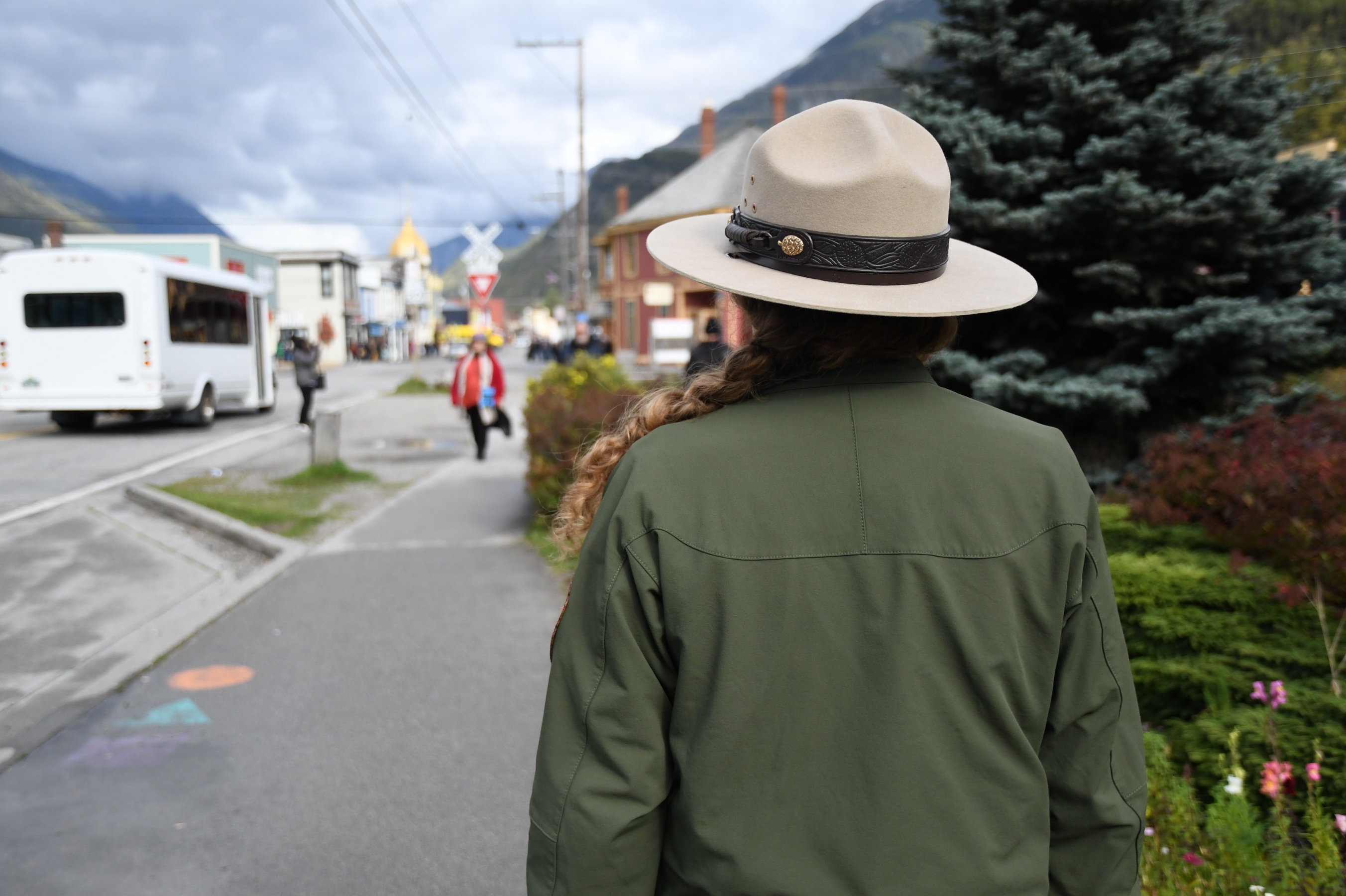 Back of ranger wearing flat hat on a street with trees in background.