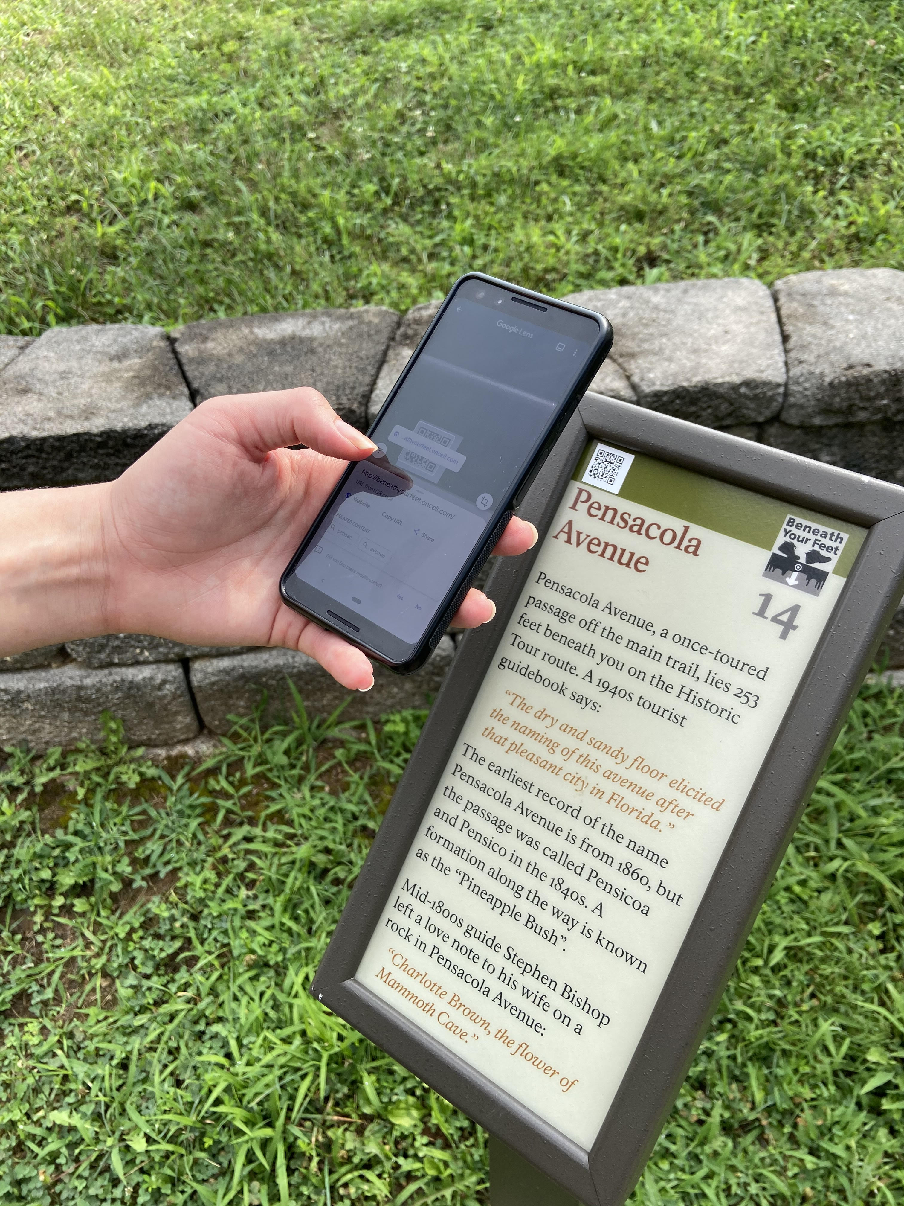 A person holding a smart phone near a wayside sign.