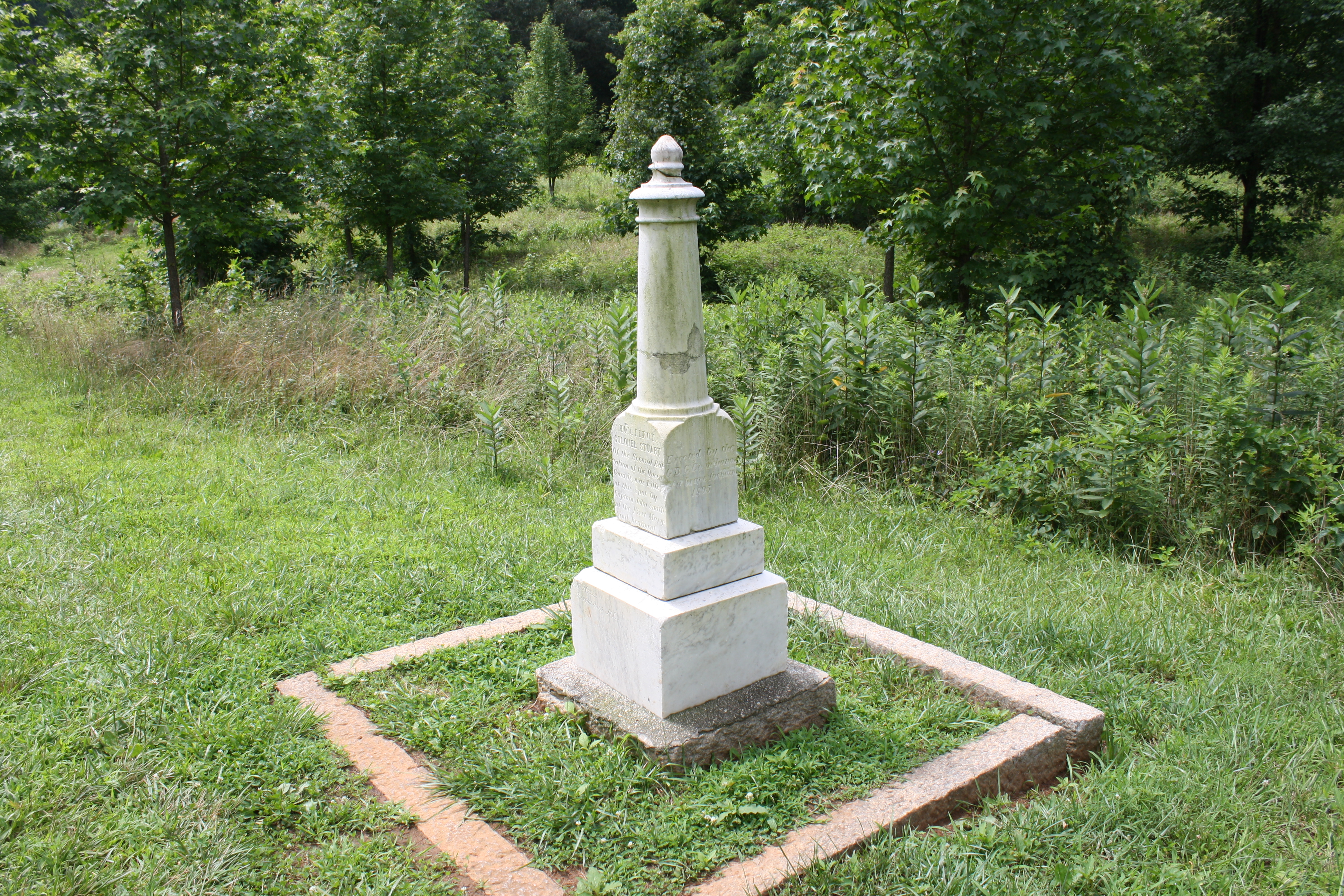 A three foot tall white Georgian marble marker shaped like a chess pawn. it stands in a green field.