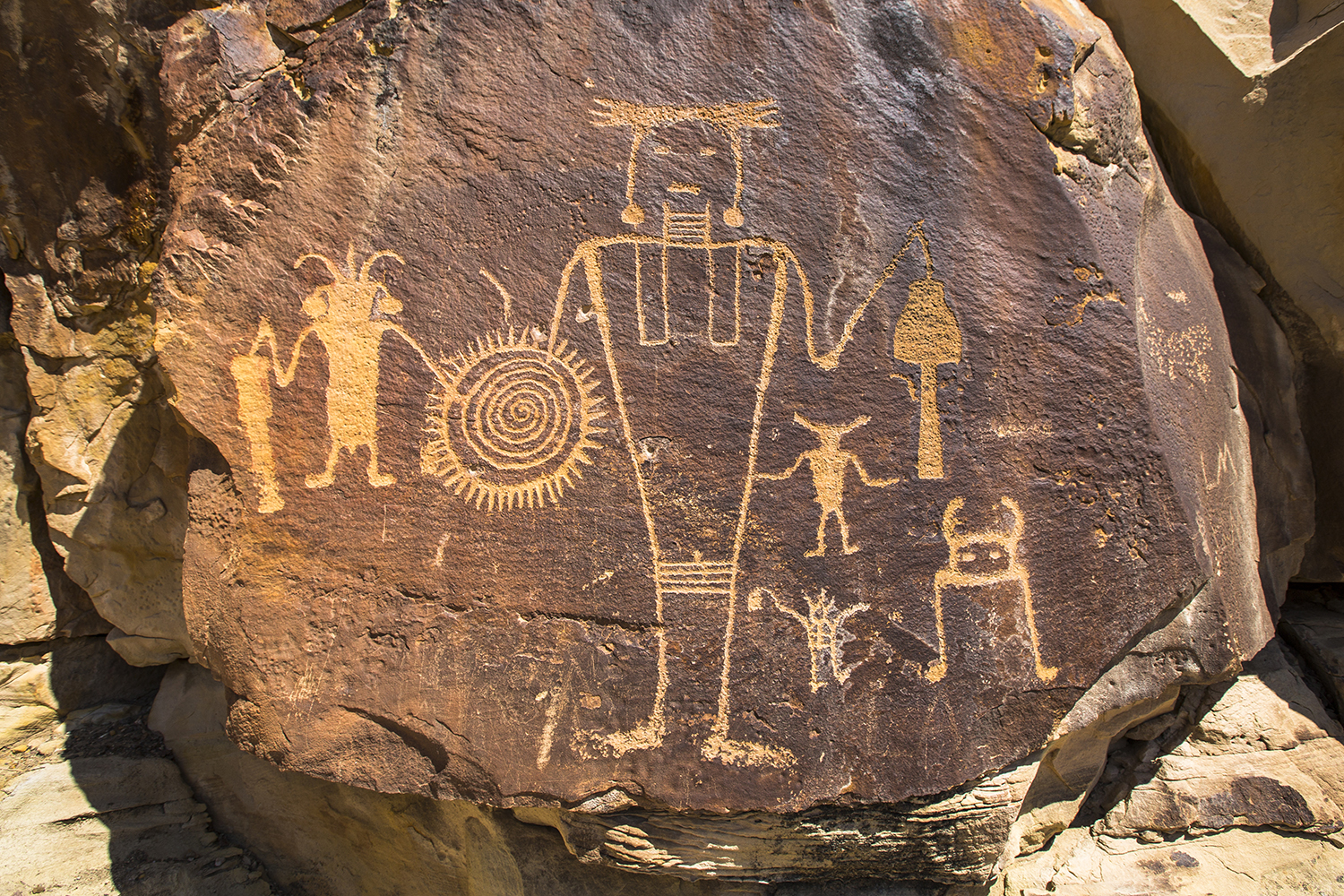 A dark orange, brown rock with human shaped carvings left by ancestral Native American peoples.