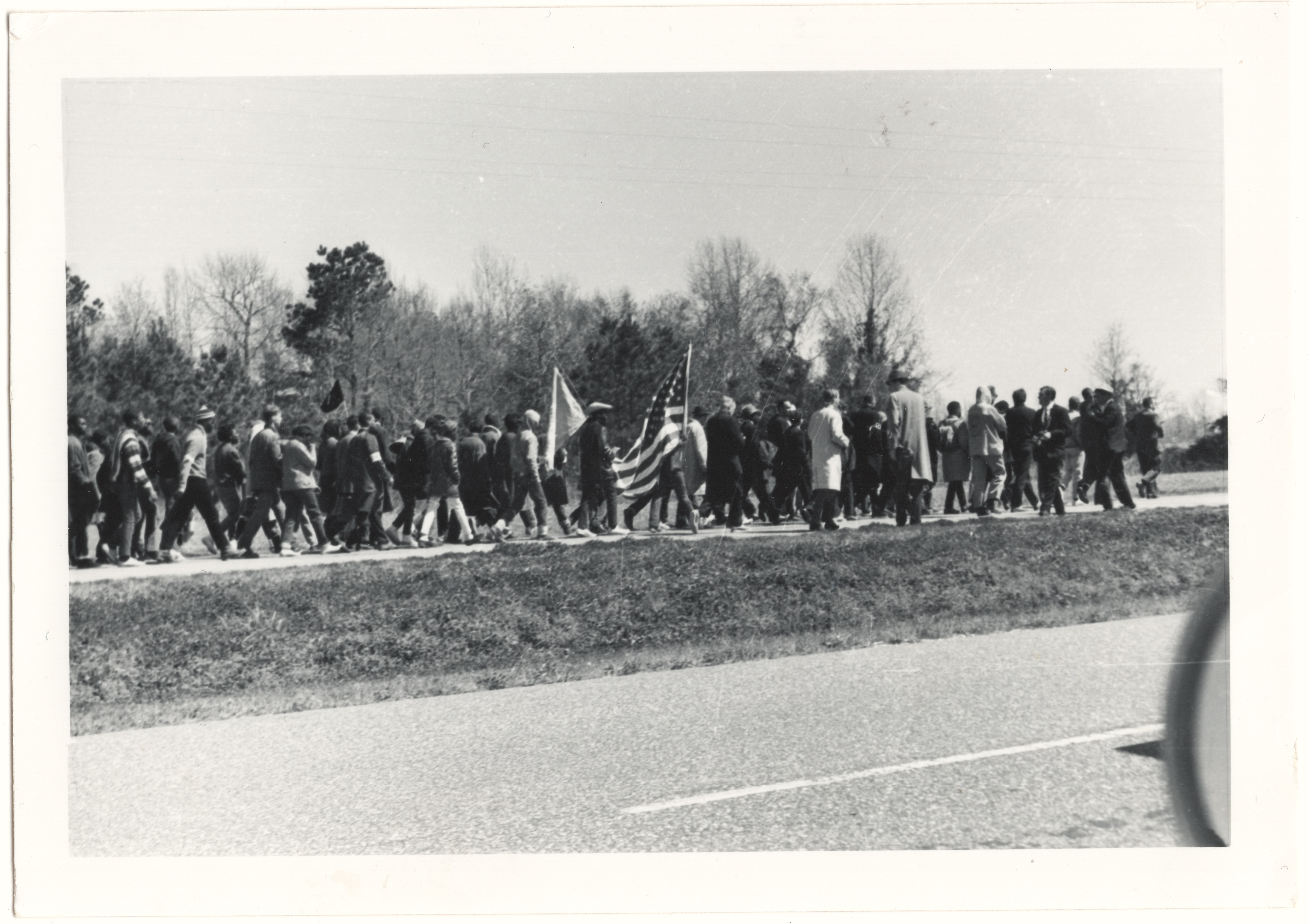 Scan of a black and white photo of a crowd of people marching on a rural highway.