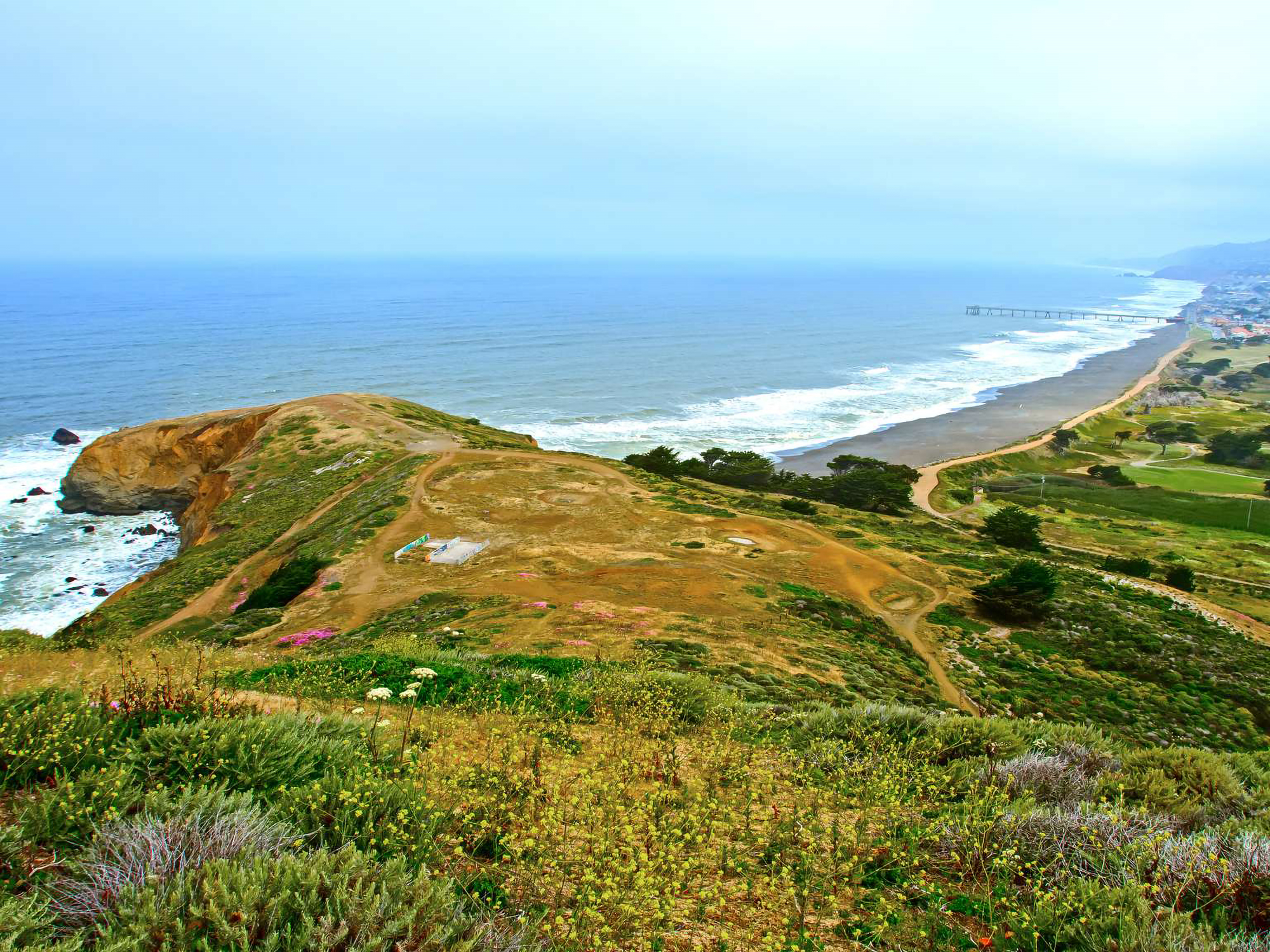 Colored photo of Mori Point covered in bright green foliage with the Pacific Ocean in the distance