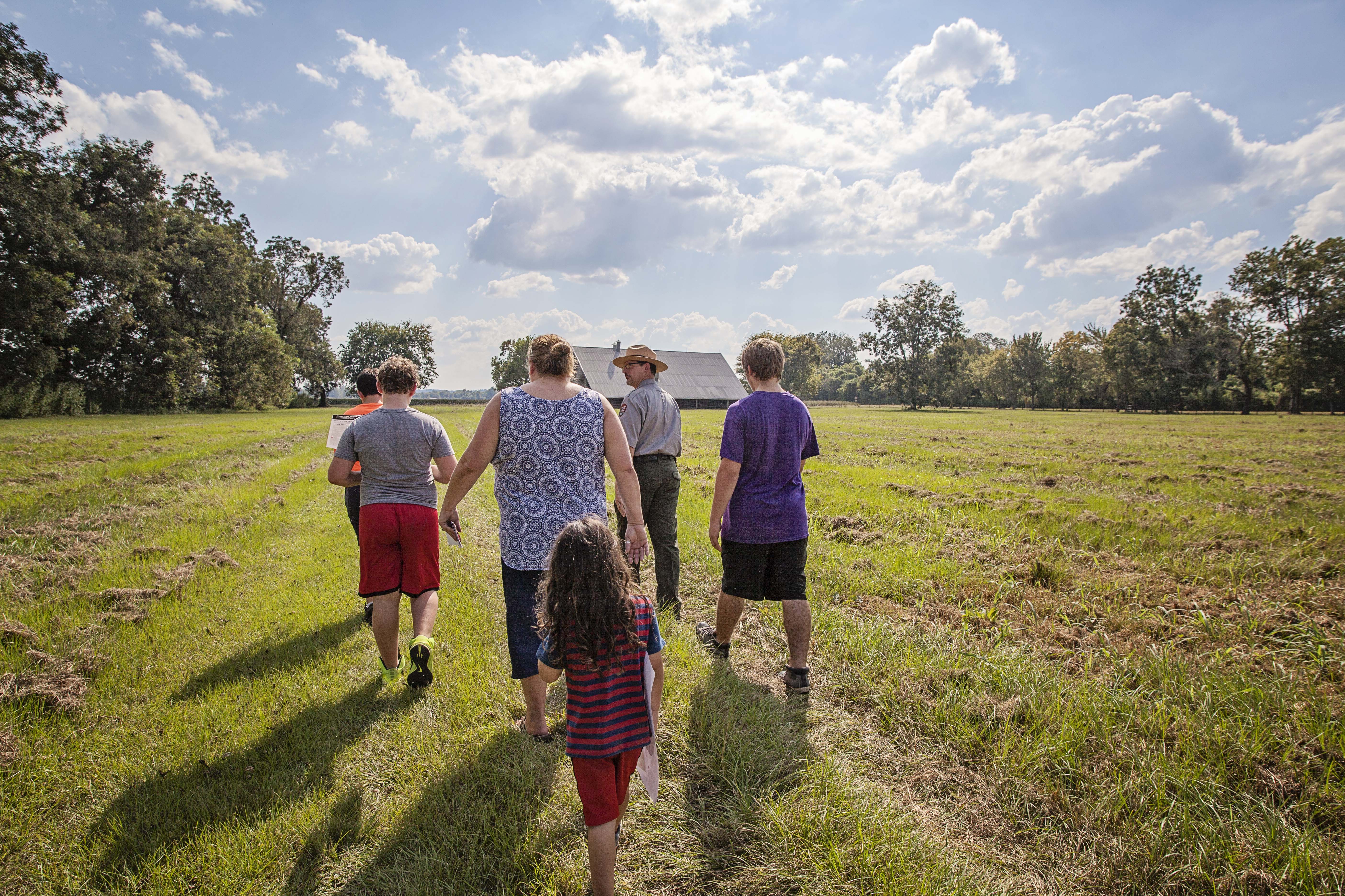 A family walking through a grassy area toward a building.