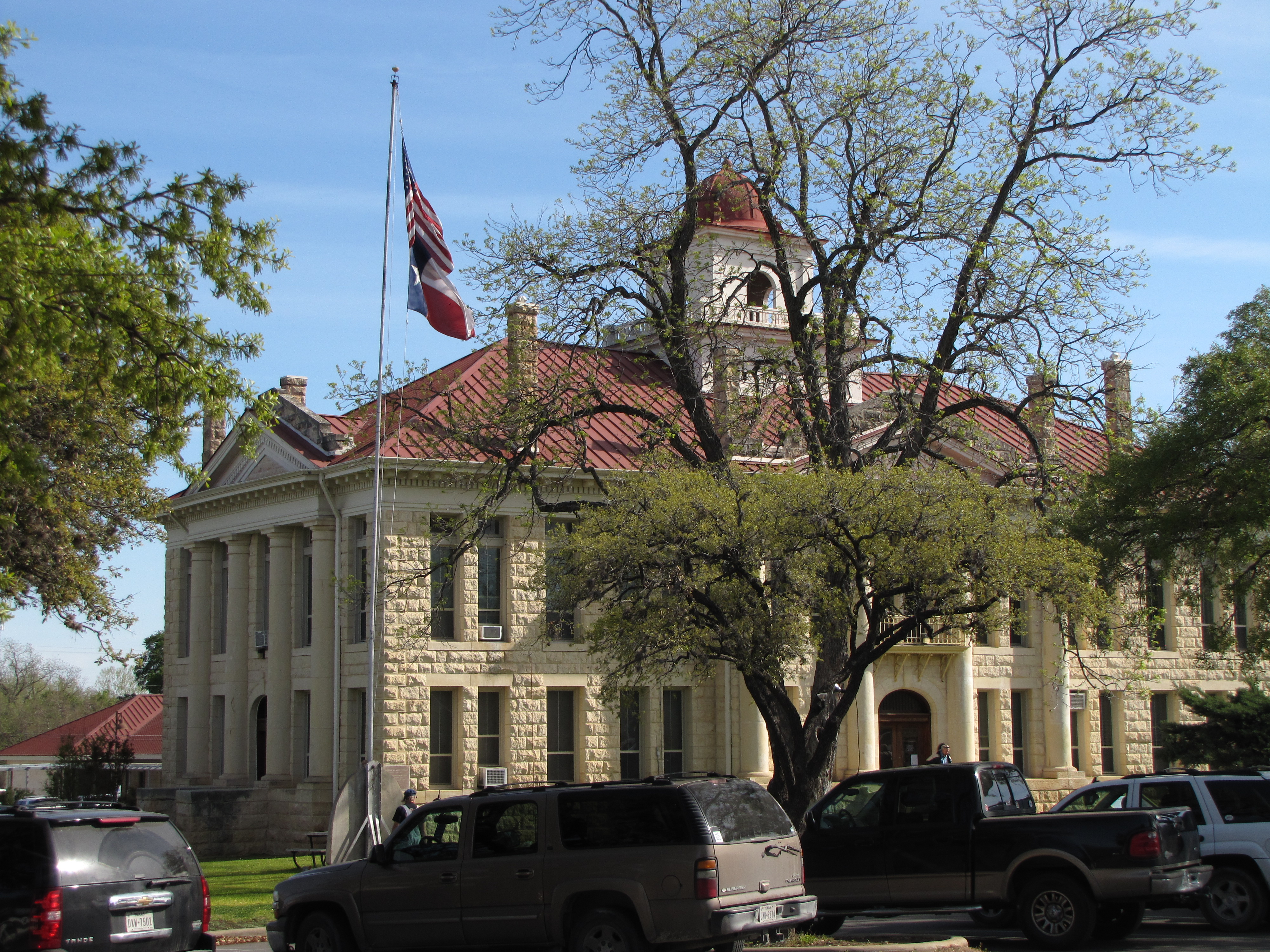 Under a blue sky, there is a large, limestone building with columns, a red roof and a domed cupola.