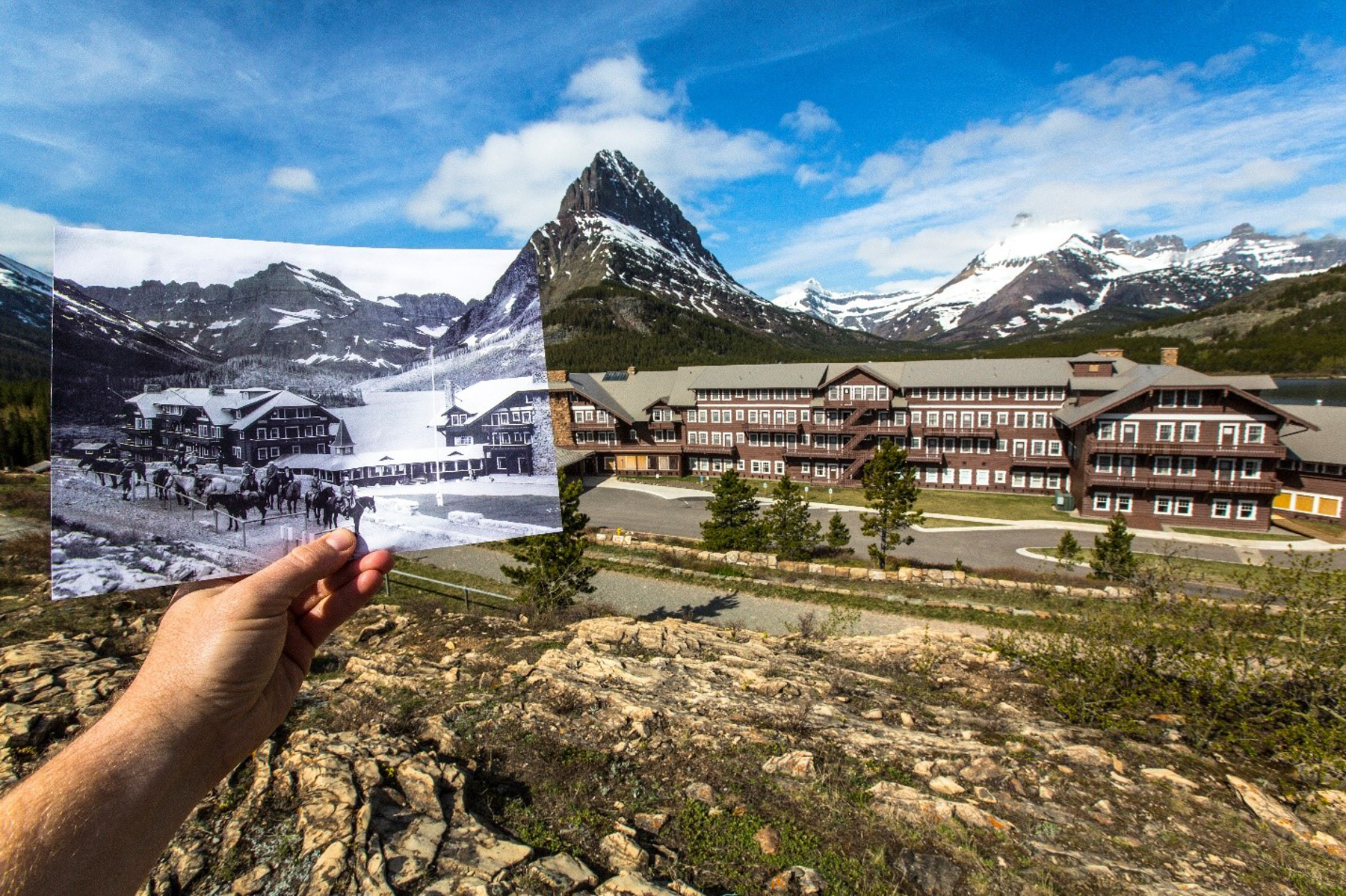 A mountain valley with chalet-style hotel. A hands holds up a historic photo of the hotel.