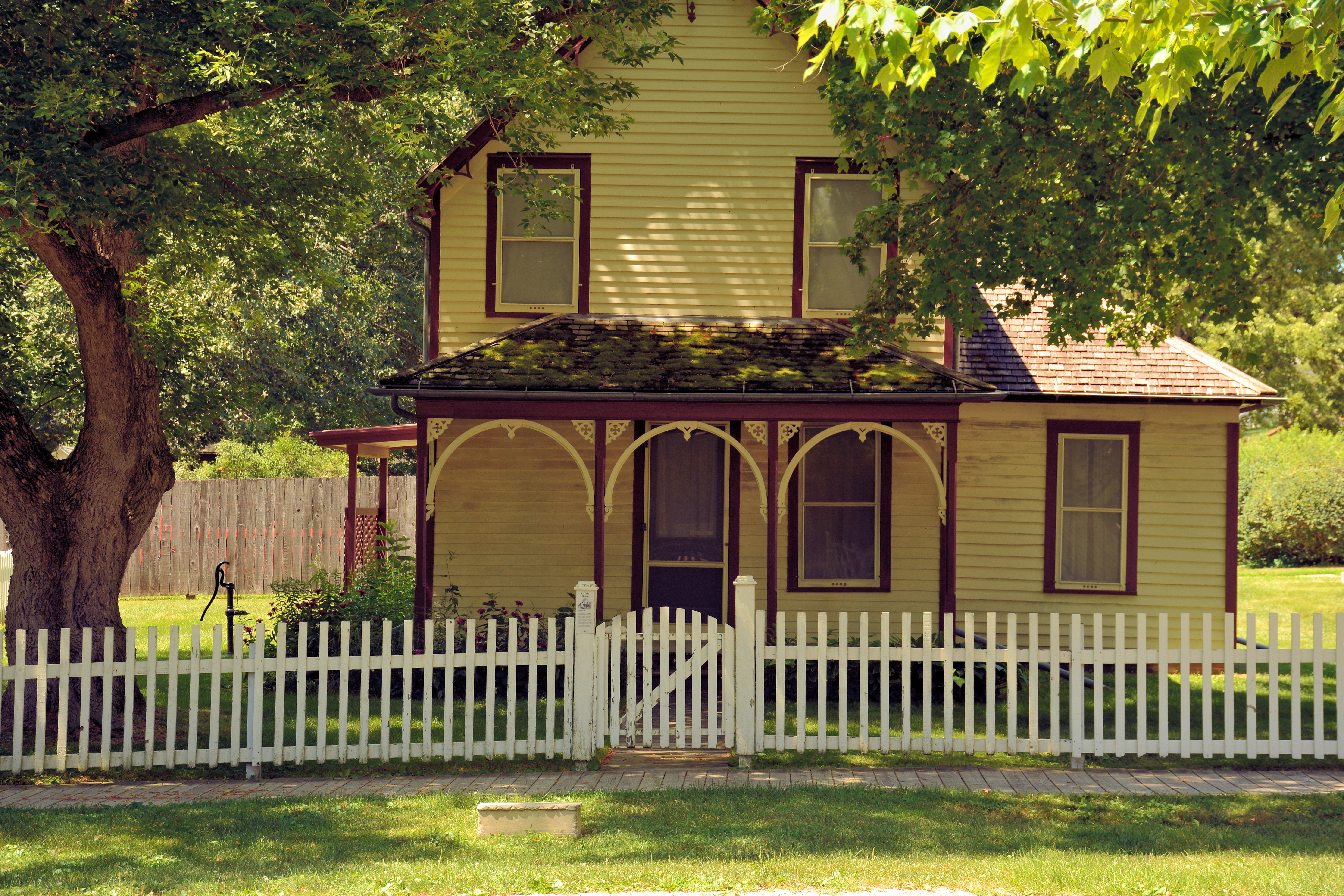 A tree filters summer sunlight onto a wood frame house with gothic arches.