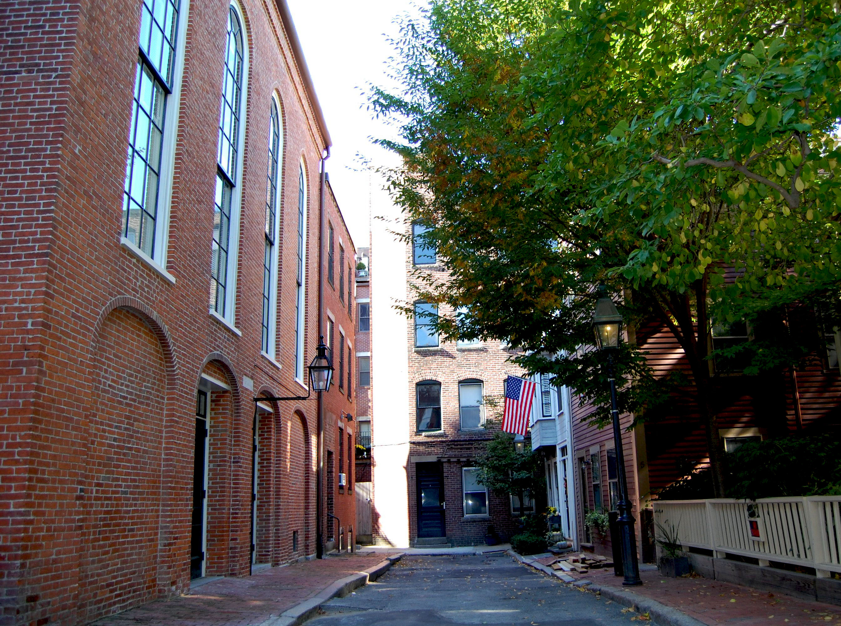 Alley with a 3-story red brick building on the left that has tall windows and homes on the right.
