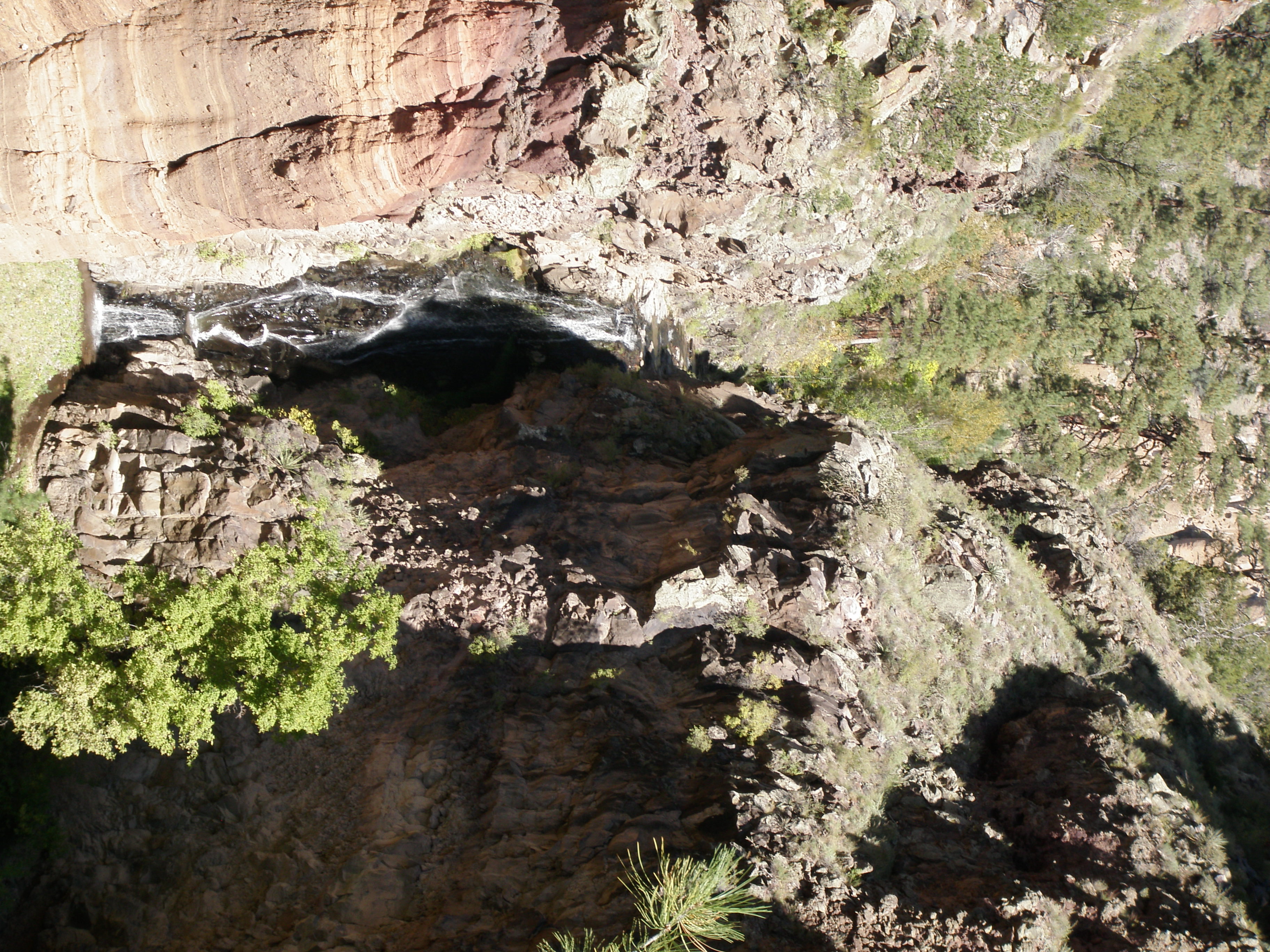 A waterfall flows down a dark cliff, with tan rock to the right and darker rock to the left.