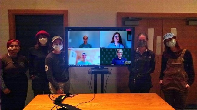 People standing alongside a TV screen with images of four people