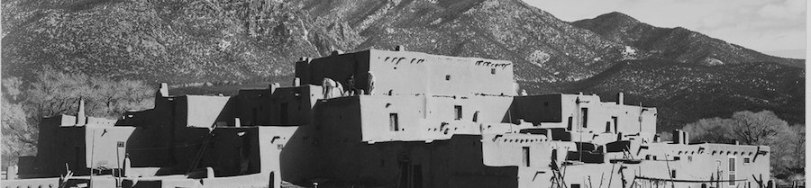 Taos A pueblo of adobe and rock with snow capped mountains in the background