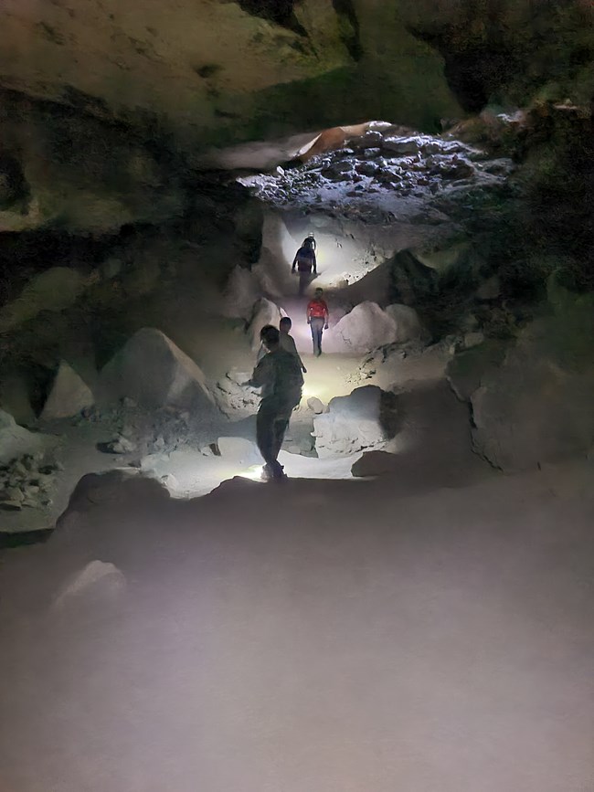 People climb over large boulders to exit the cave