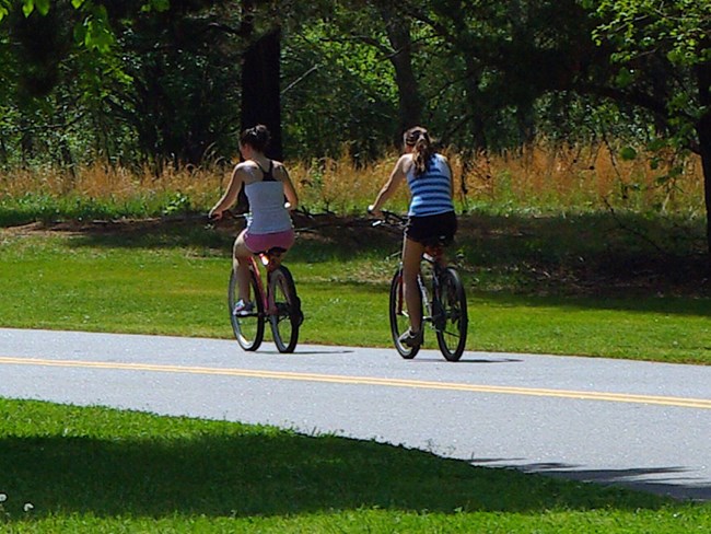 2 girls ride on the Loop Road, away from the viewer