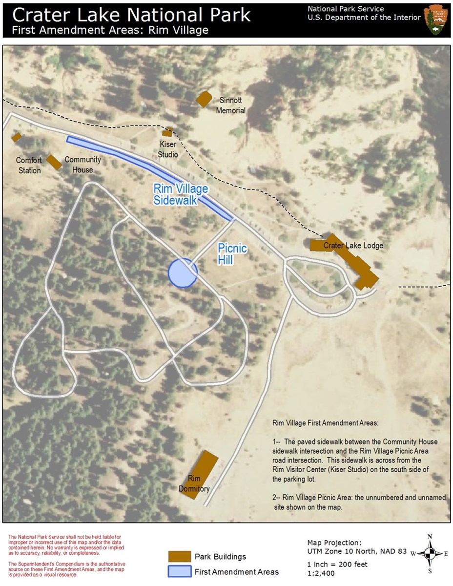 Map of Rim Village. Roads are white. Five buildings are brown. A dashed line is the Rim Village Promenade. A long blue area and a blue-filled circle show the locations of First Amendment Areas for free speech.